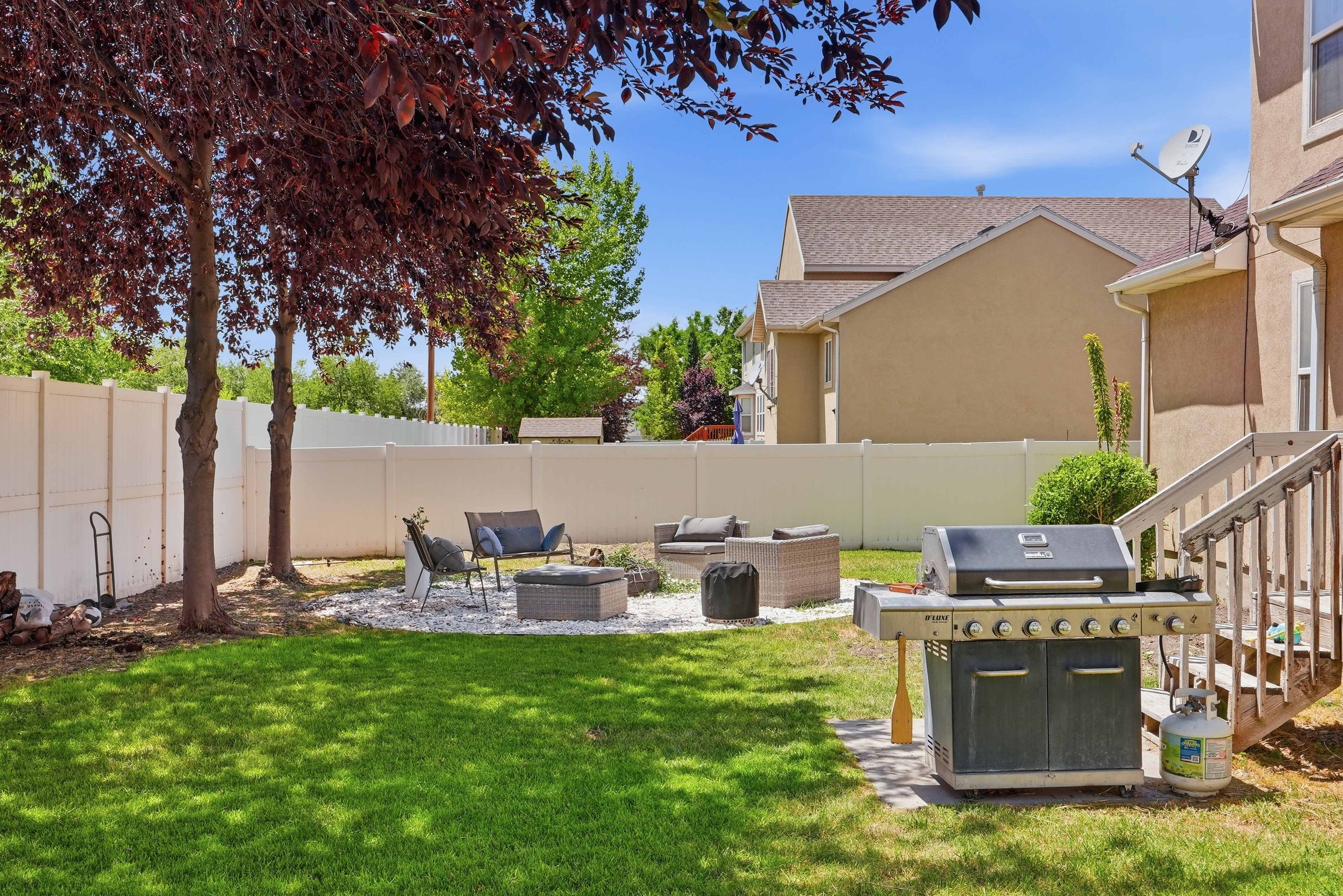 Expansive green lawn featuring mature trees and a white privacy fence
