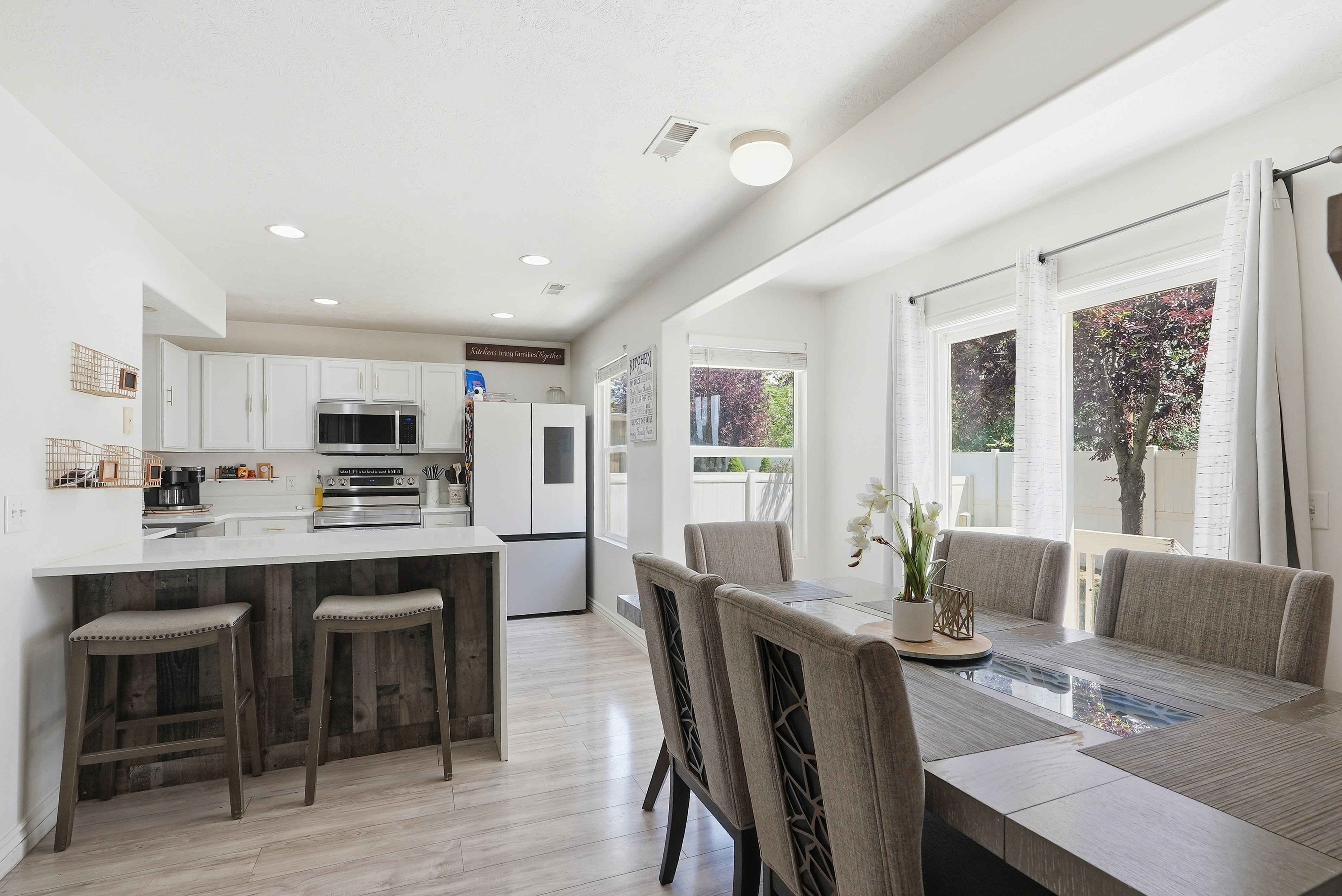 Open-concept kitchen and dining area featuring white cabinetry, stainless steel appliances, and a wood-finish breakfast bar