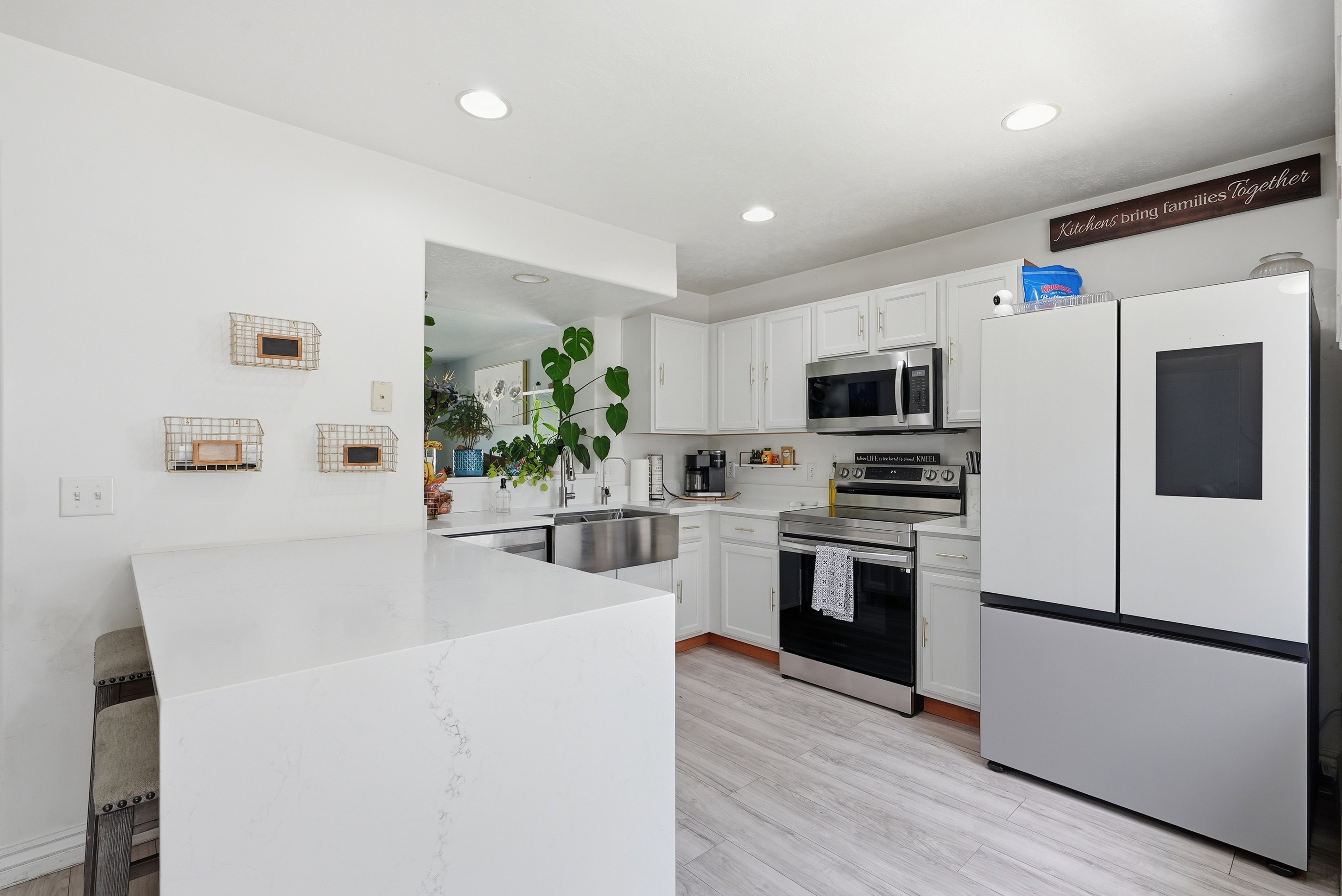 Kitchen featuring white cabinetry, light-toned wood-finish flooring, recessed lighting, stainless steel appliances, and a waterfall-edge island with seating