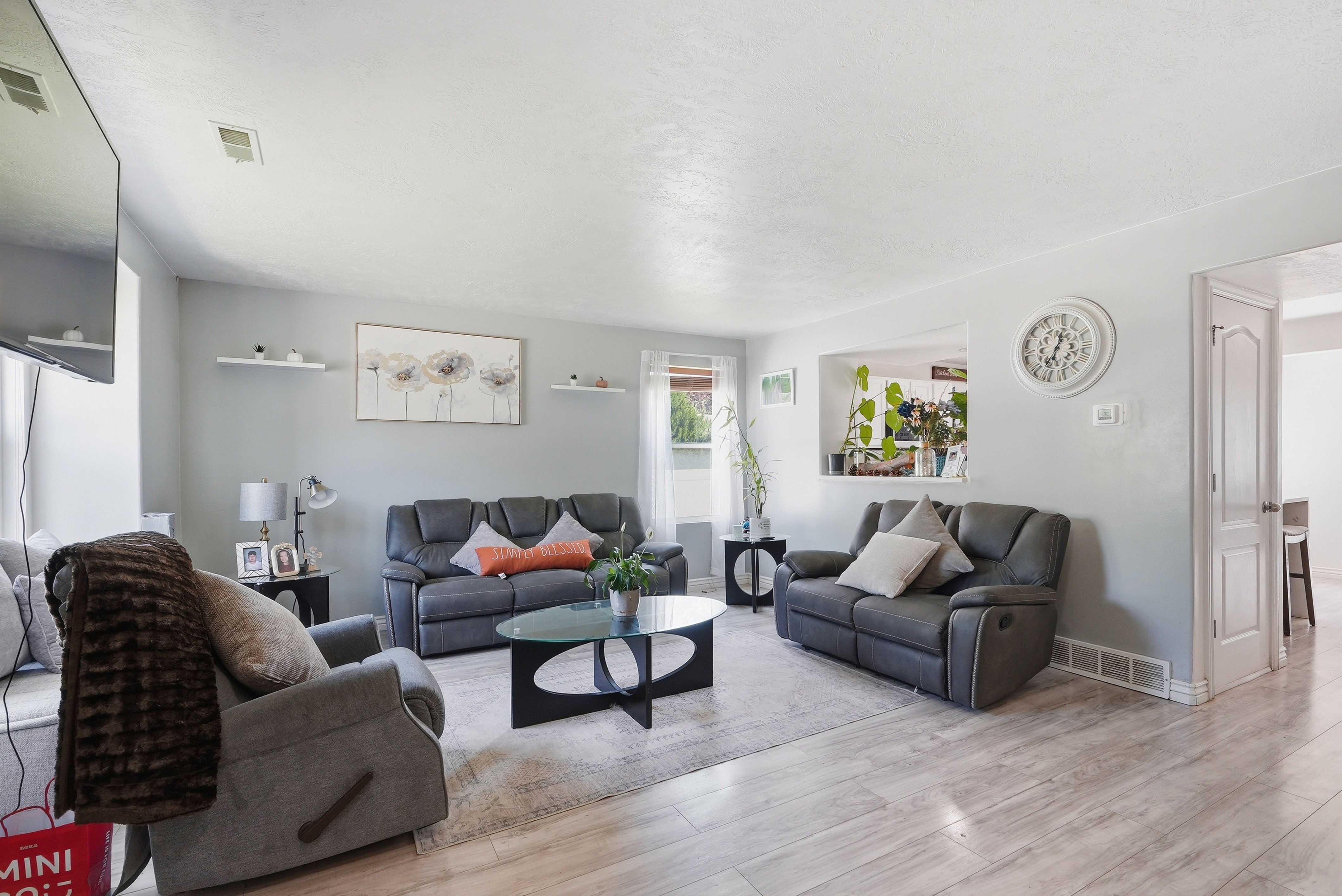 Spacious living room featuring light wood-finish flooring, neutral paint palette, and a decorative pass-through opening