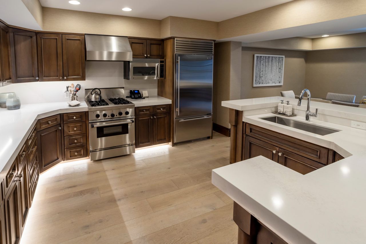 Gourmet kitchen featuring dark wood cabinetry, white countertops, stainless steel appliances including a range with a hood, a large refrigerator, and a built-in microwave
