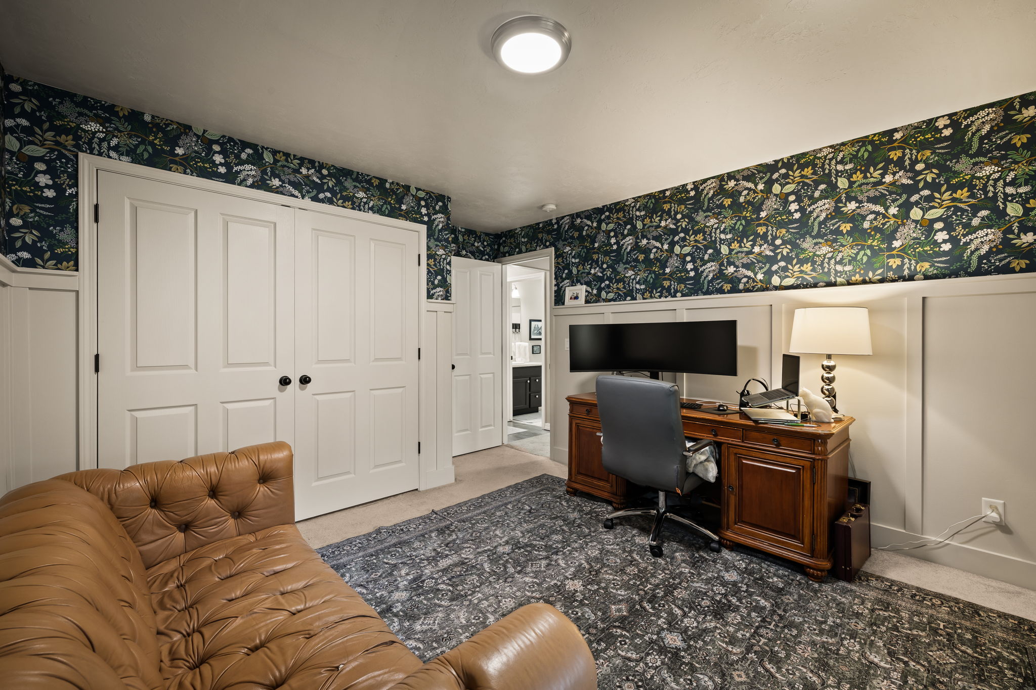 Interior room featuring white board and batten wainscoting with botanical wallpaper, ceiling-mounted lighting, and paneled doors