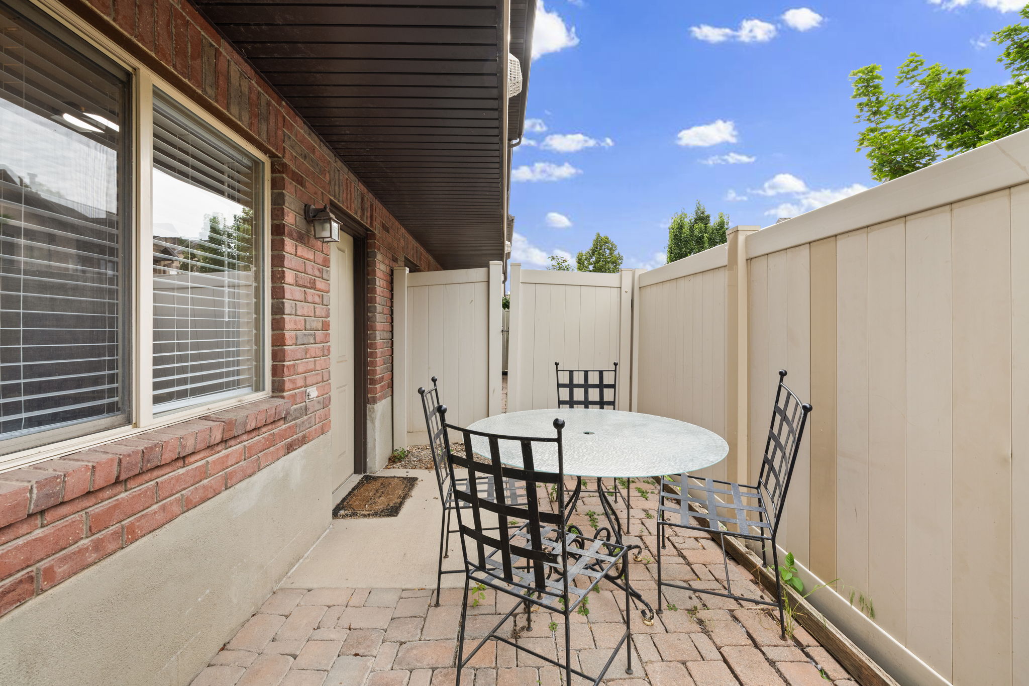 Private brick paver patio area featuring a red brick exterior, a secure privacy fence, and an exterior wall light fixture