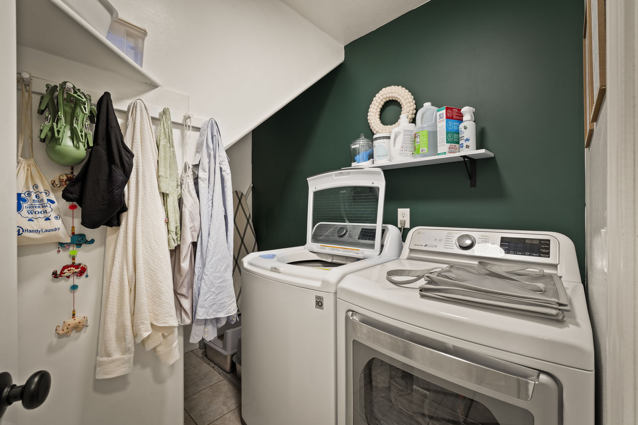 Dedicated laundry space featuring a rich green accent wall, white cabinetry, a built-in shelving unit, and tile flooring