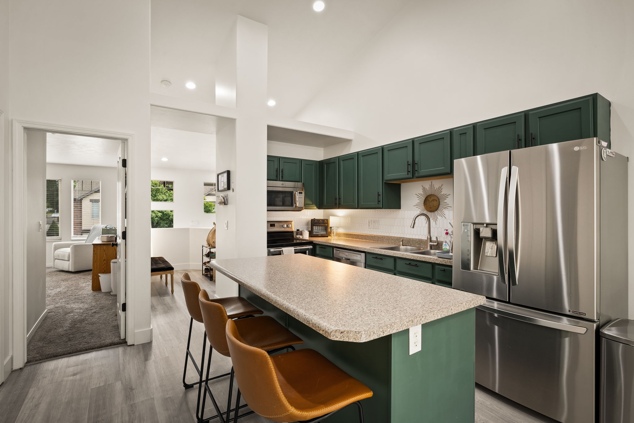 Kitchen featuring green cabinetry, stainless steel appliances, a white subway tile backsplash, and a breakfast bar with a light-colored countertop