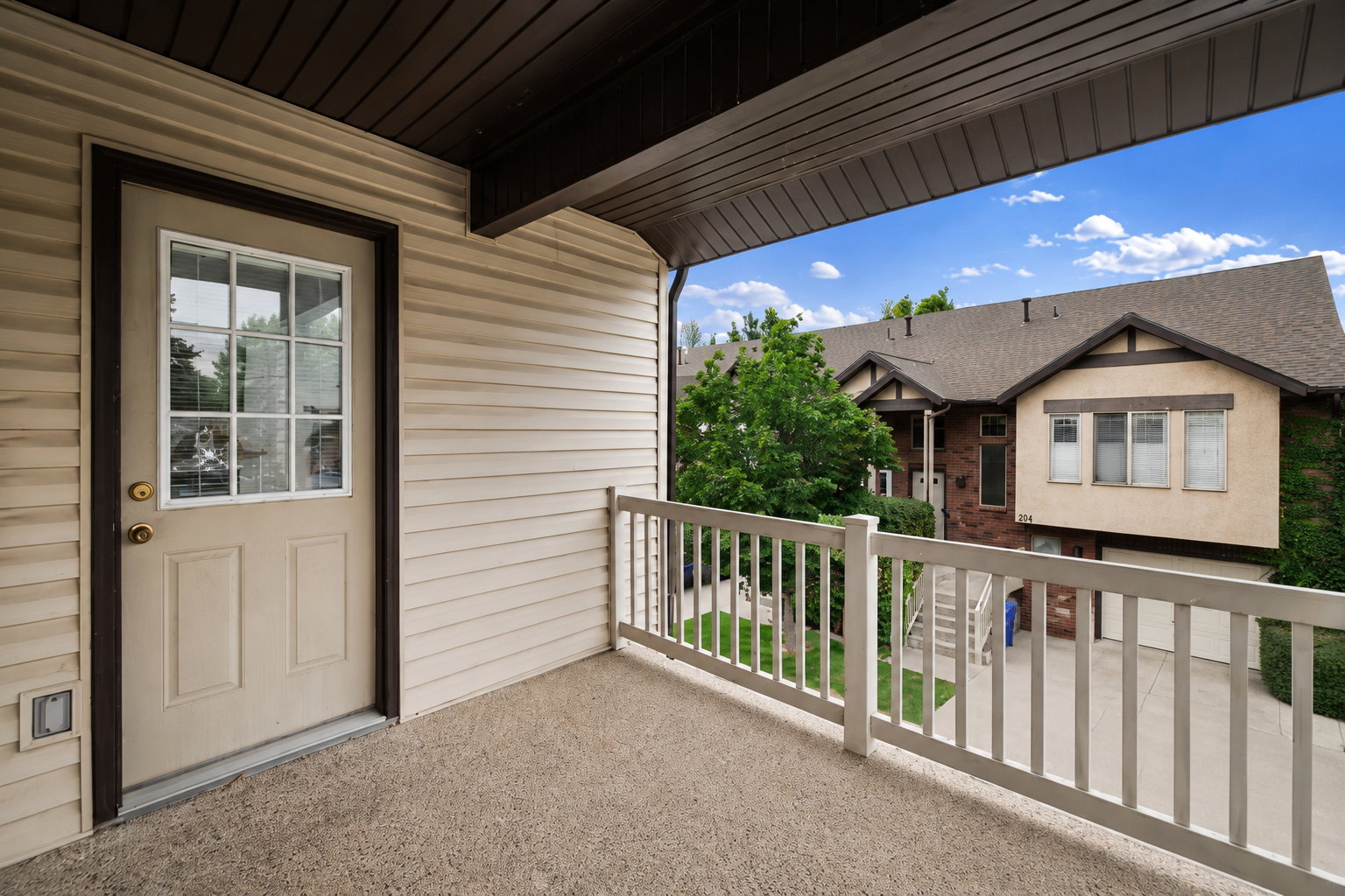 Private outdoor balcony featuring a textured concrete surface, white railing, and exterior wall with horizontal siding