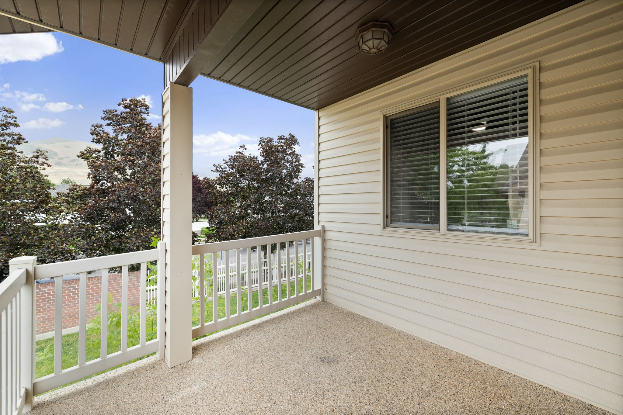 Covered outdoor patio featuring a textured concrete surface, white railing, and a window with blinds
