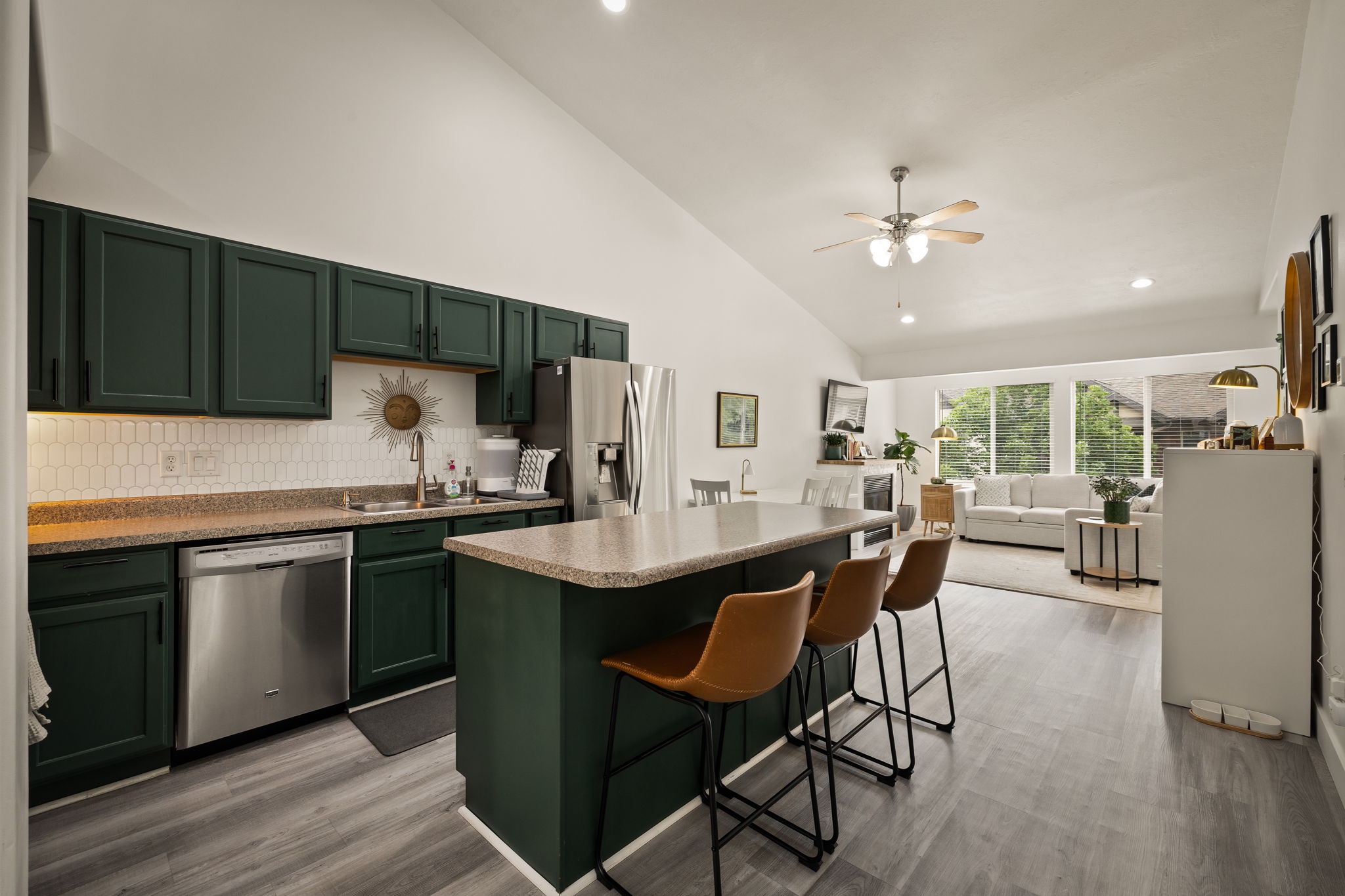 Open-concept kitchen featuring dark green cabinetry, stainless steel appliances, and a central island with bar seating