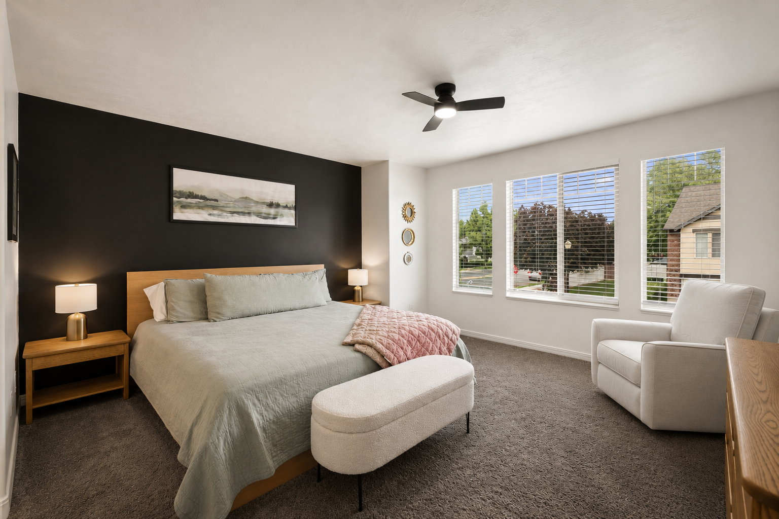 Spacious room featuring a dark accent wall, three large windows with blinds, a ceiling fan, and carpeted flooring