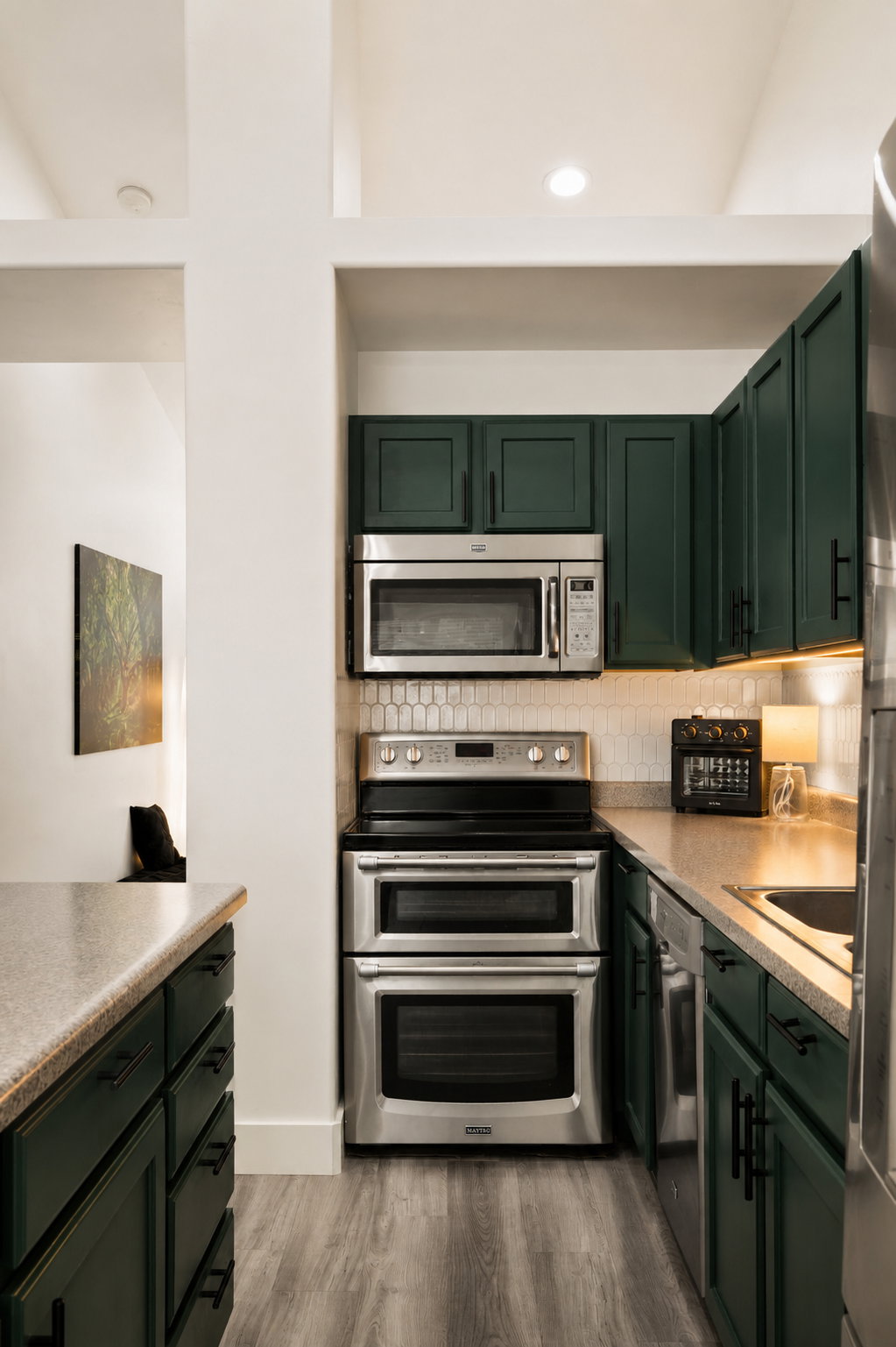 Kitchen featuring dark green cabinetry with matte black hardware, stainless steel appliances, light wood-finish flooring, and light-toned countertops