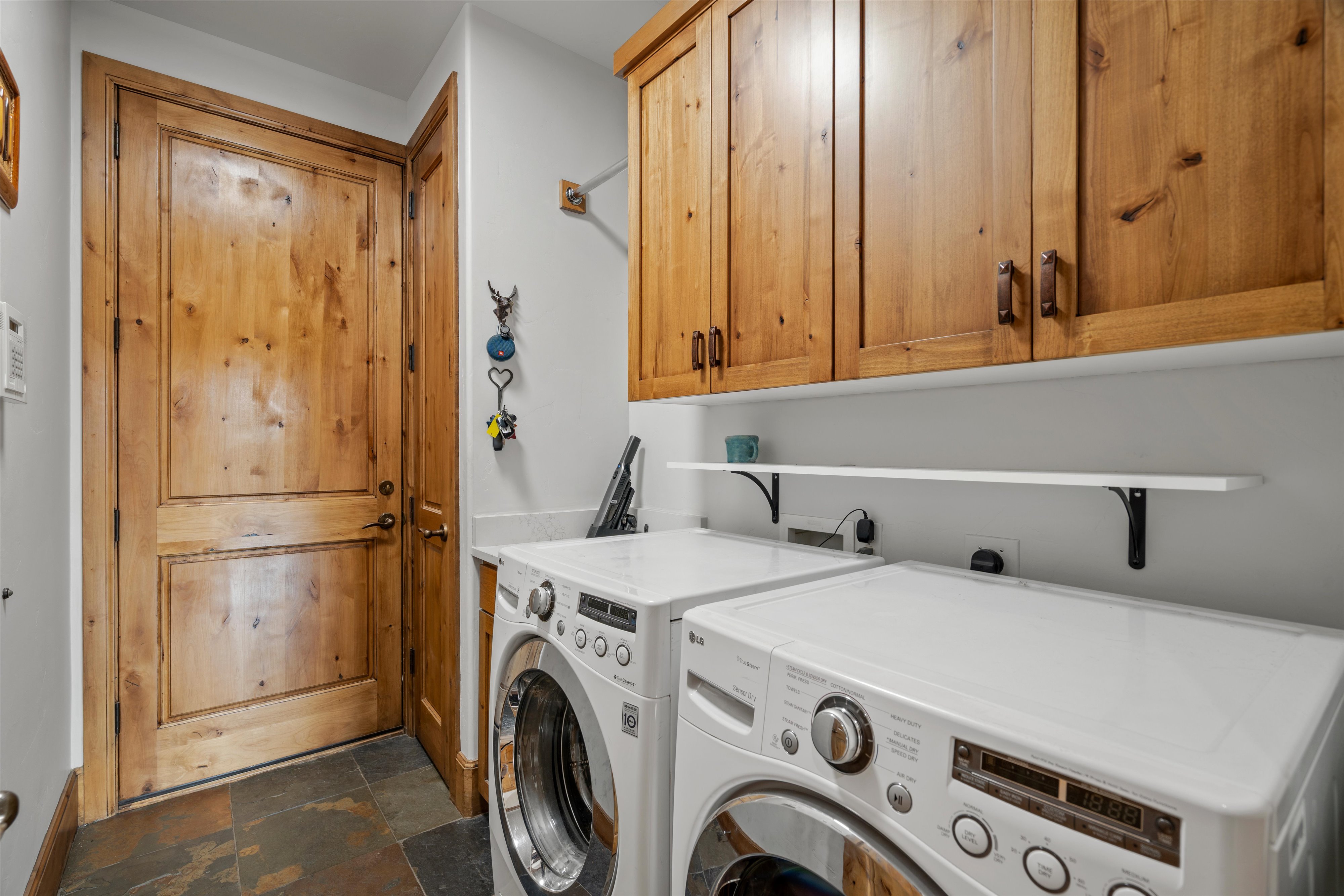 Laundry area with slate tile flooring, wood-paneled door, and natural wood cabinetry