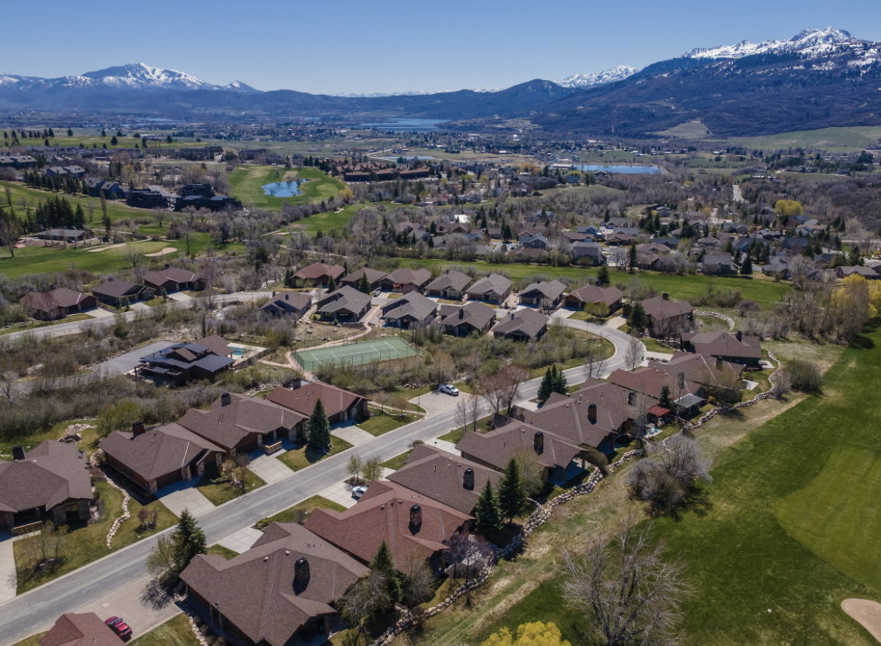Expansive community featuring numerous single-family residences with brown-tone roofs, a visible tennis court, and a nearby golf course