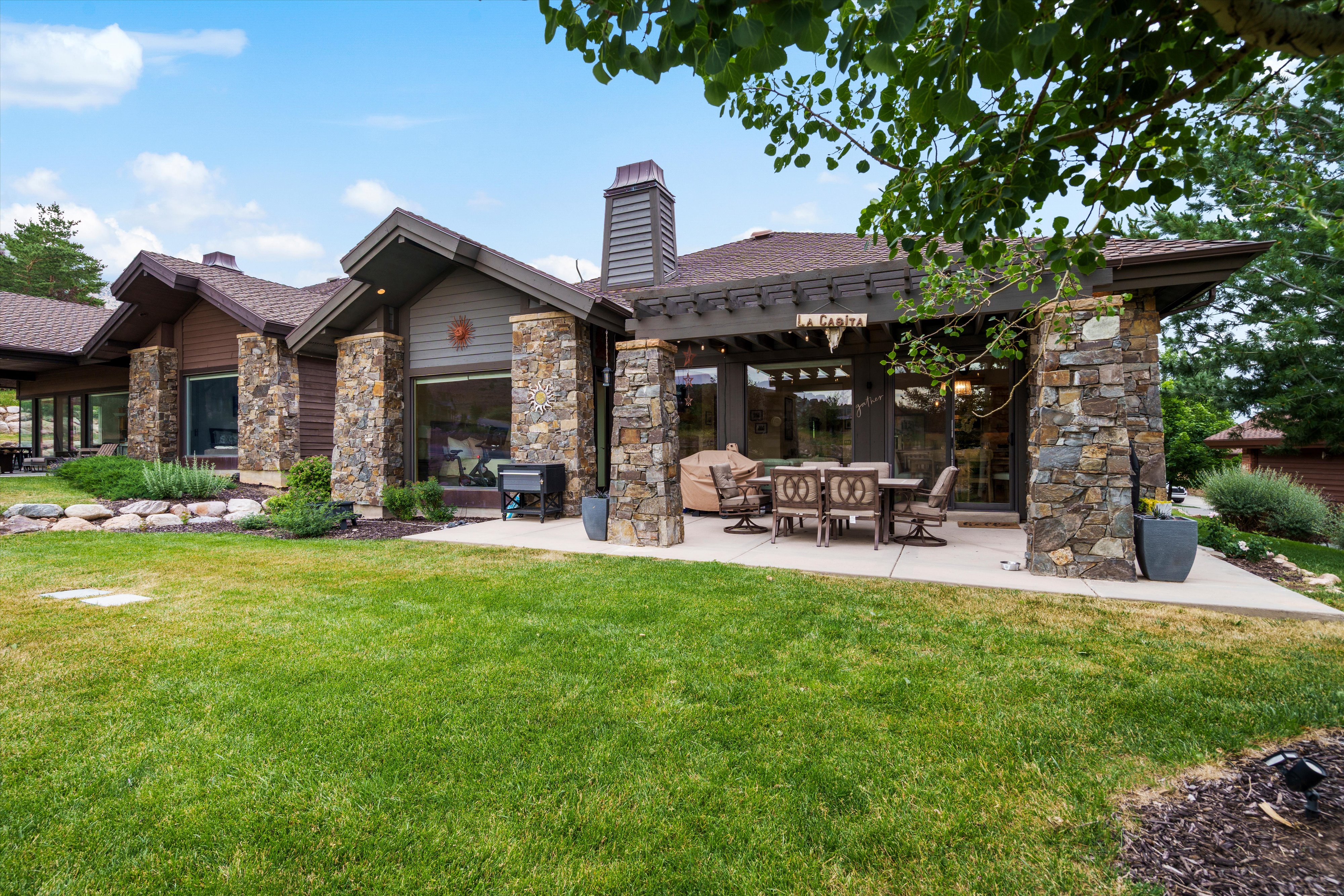 Stone and wood-sided exterior featuring multiple large windows, a covered patio with a pergola, and an expansive lawn