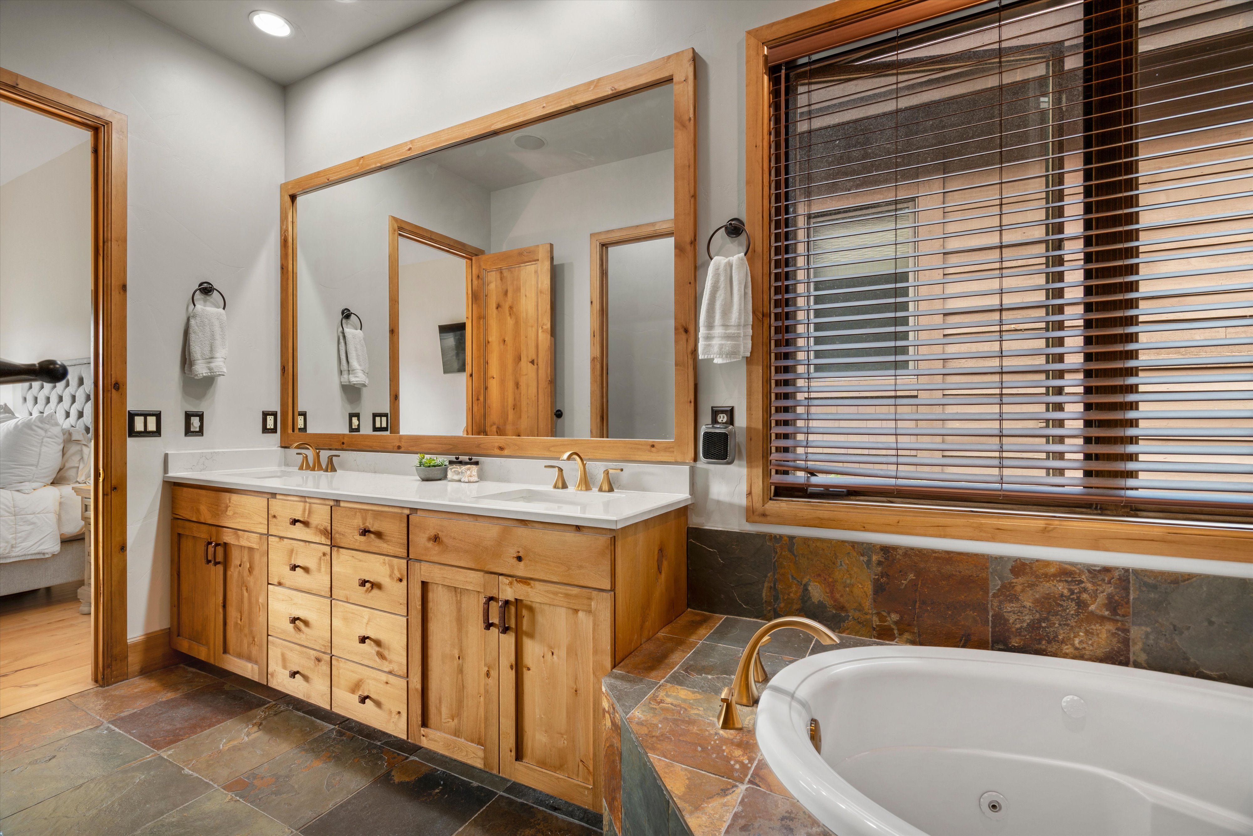 Dual sink vanity with wood cabinetry and white countertops, a large framed mirror, recessed lighting, and a window with wood blinds