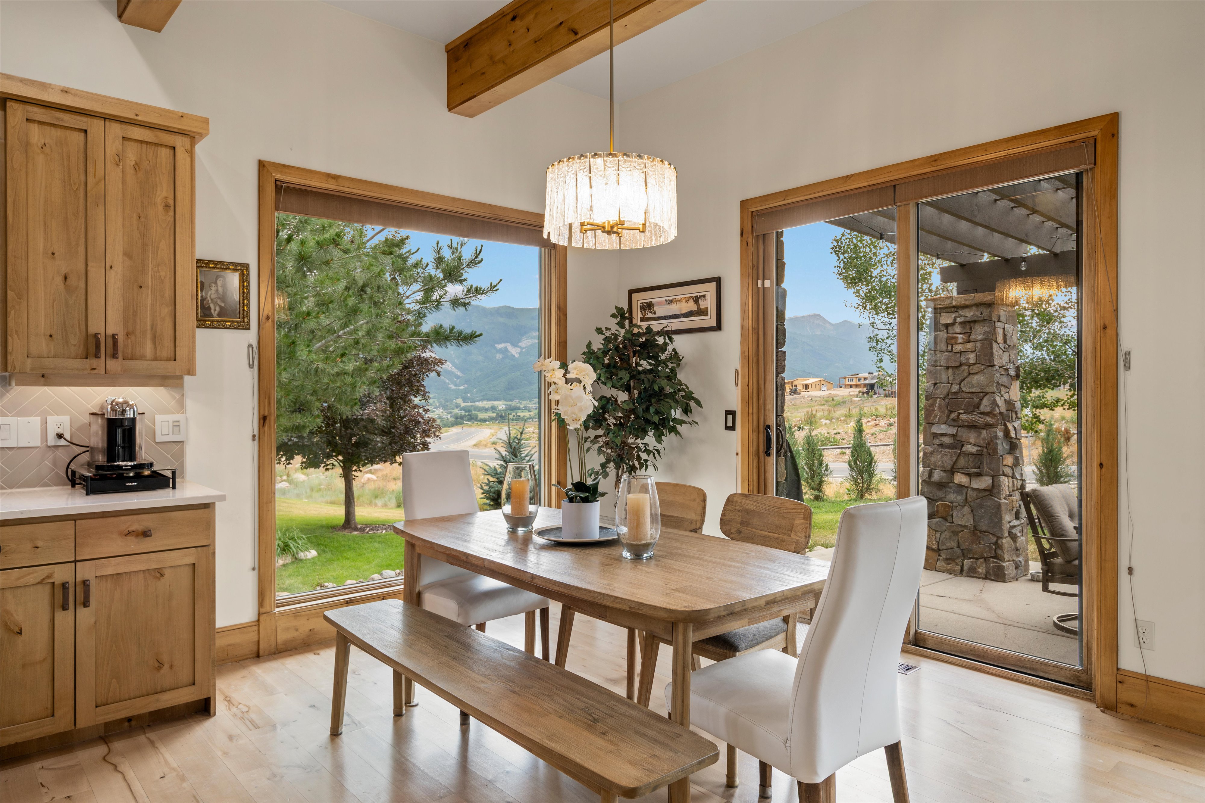 Open-concept dining area featuring wood-finish flooring, exposed wood ceiling beams, and a contemporary chandelier