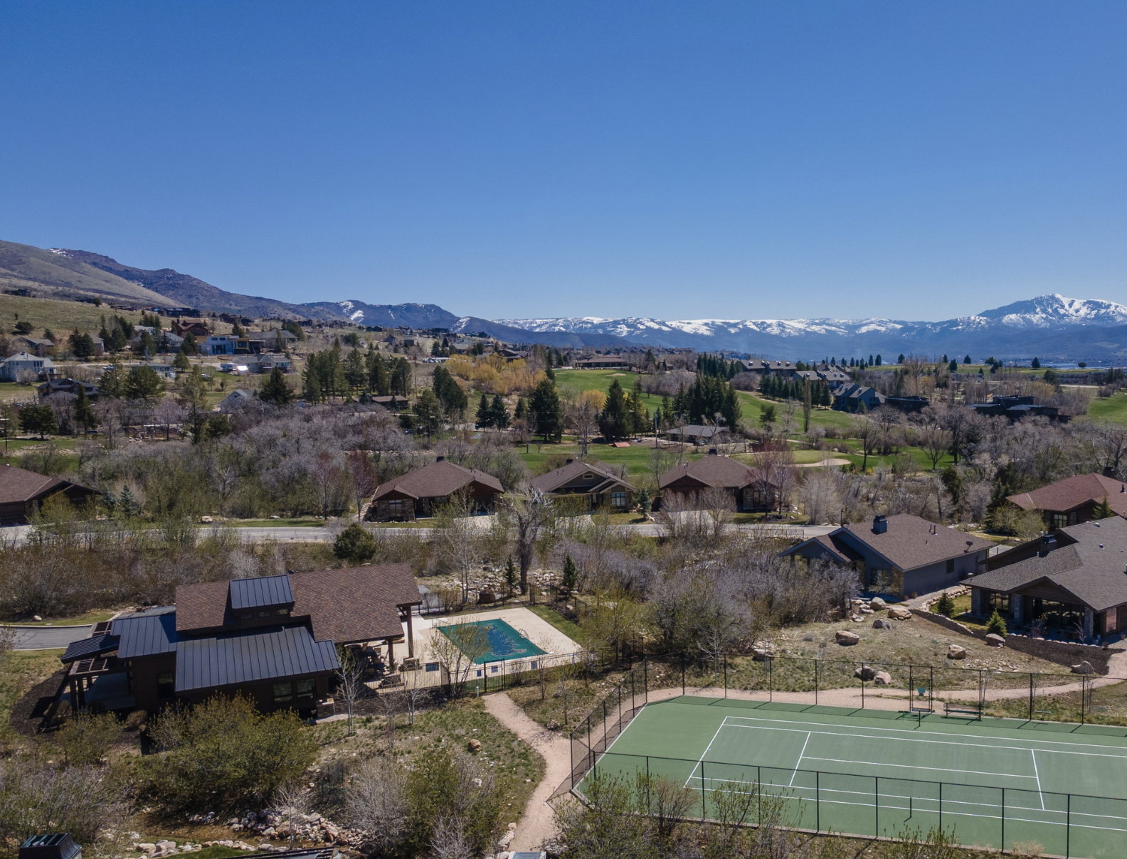 Hardscaped tennis court and fenced swimming pool with surrounding natural landscaping