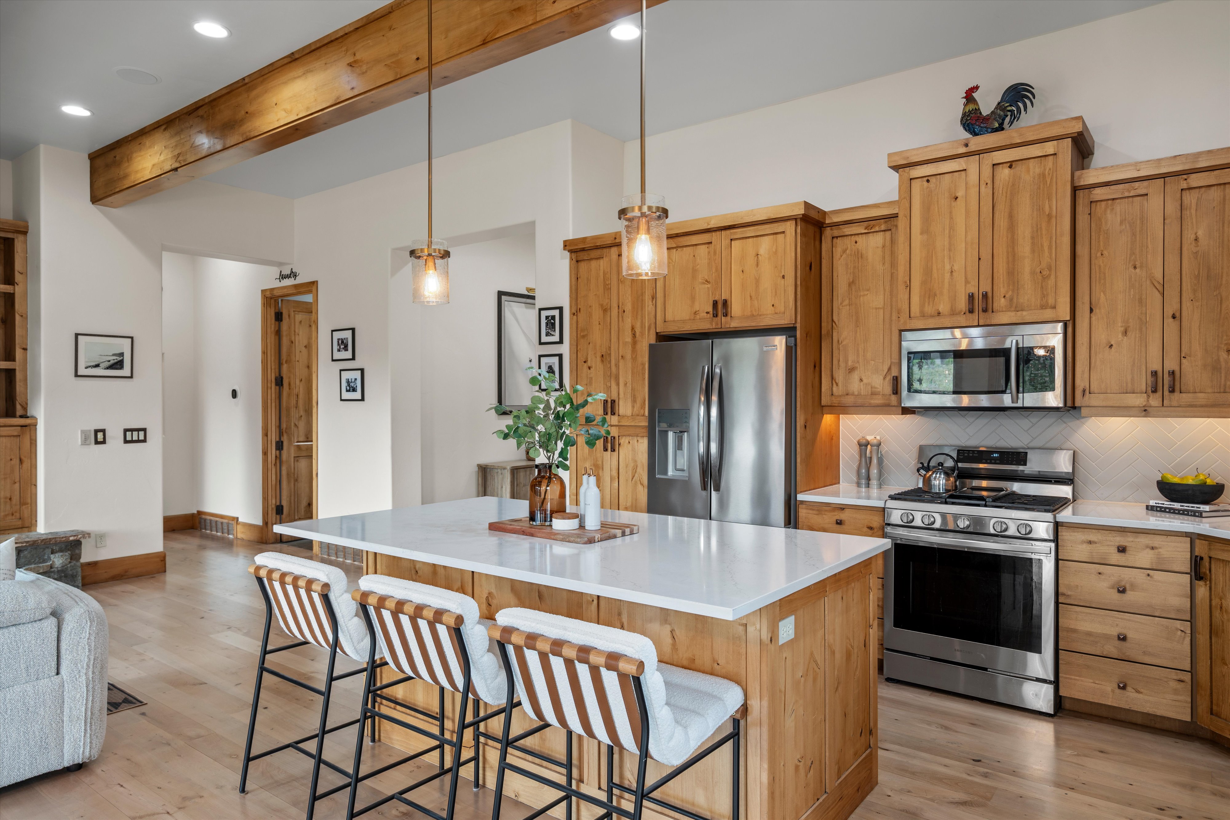 Well-appointed kitchen featuring light wood cabinetry, stainless steel appliances, a white countertop island, pendant lighting, and light wood-finish flooring