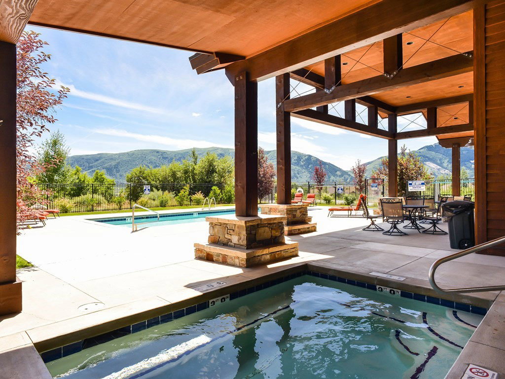 Covered patio area at the HOA clubhouse featuring a built-in hot tub, concrete decking, exposed wood beams, and stone accents