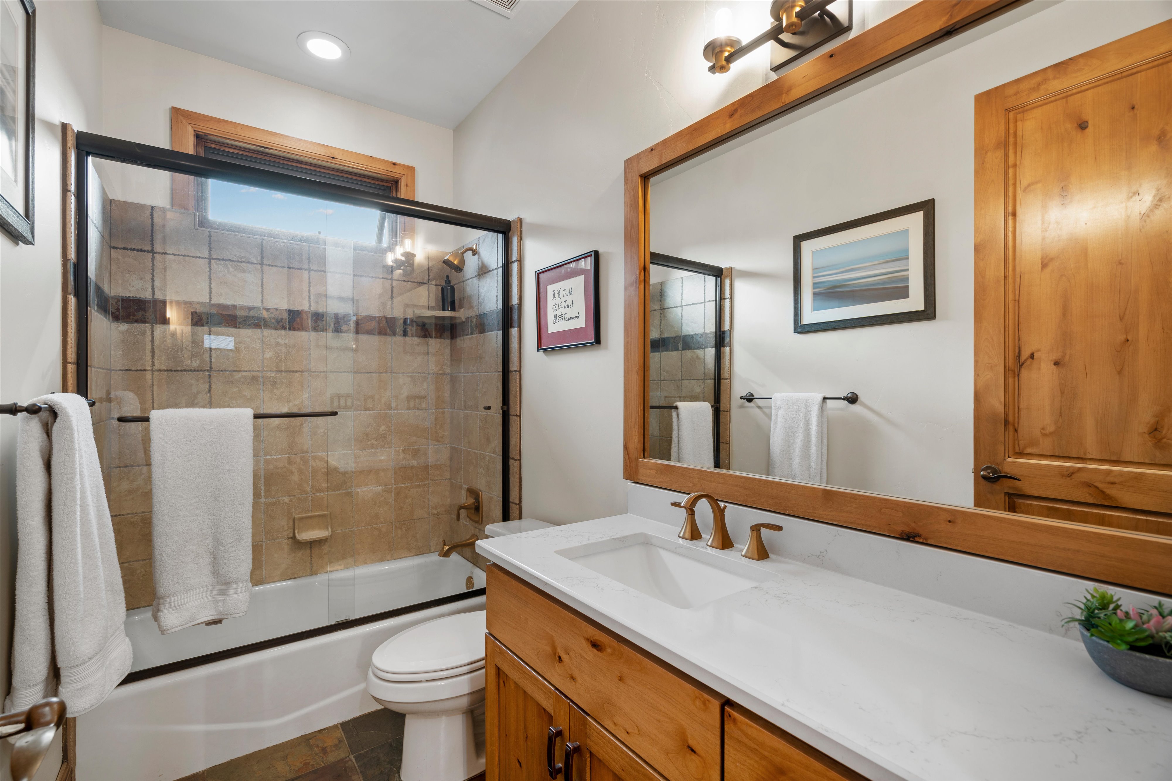 Bathroom featuring a natural wood vanity with a white countertop and undermount sink, bronze-finish faucet, and a large wood-framed mirror