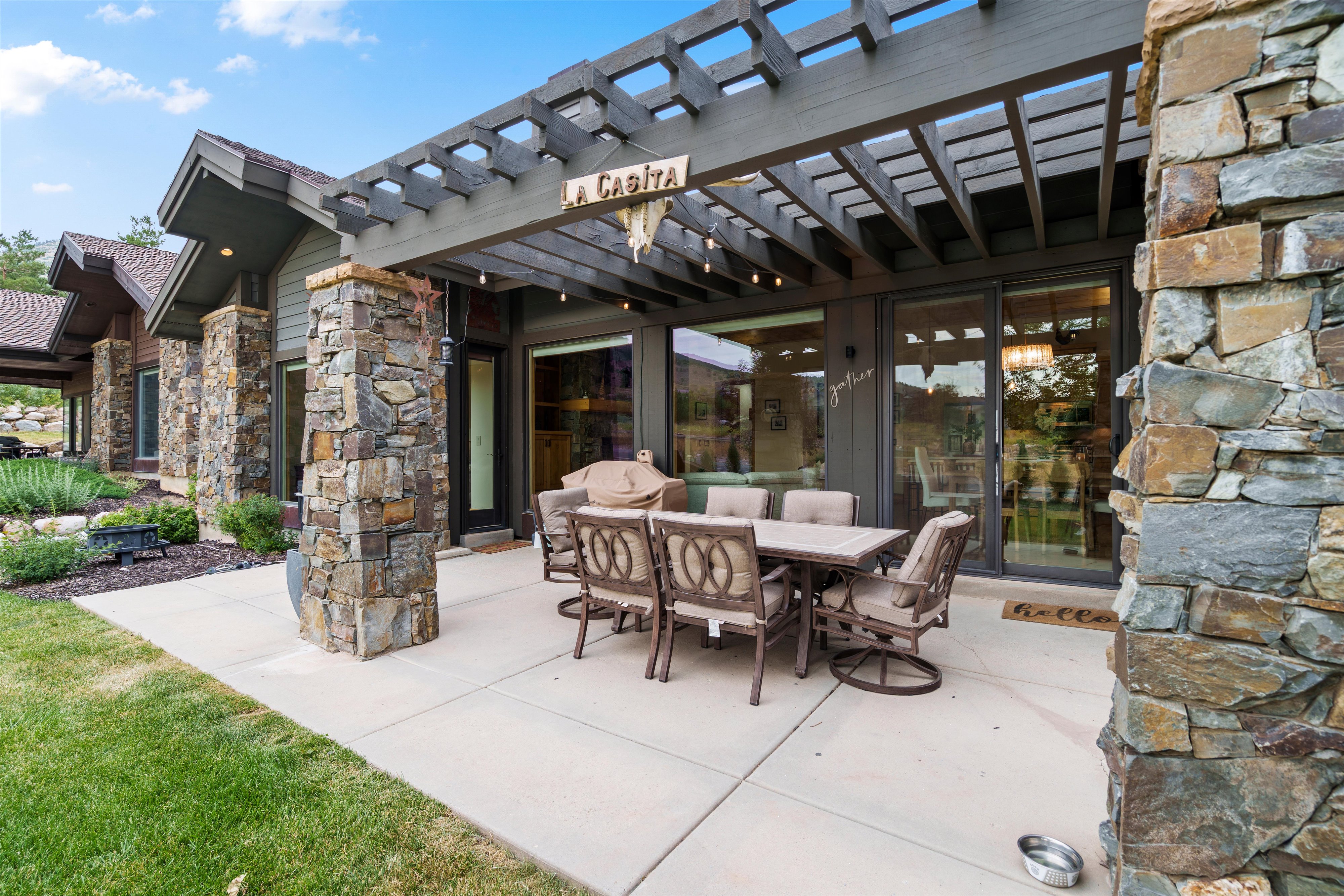 Expansive outdoor living area featuring a concrete patio, a dark wood pergola, and stone pillars