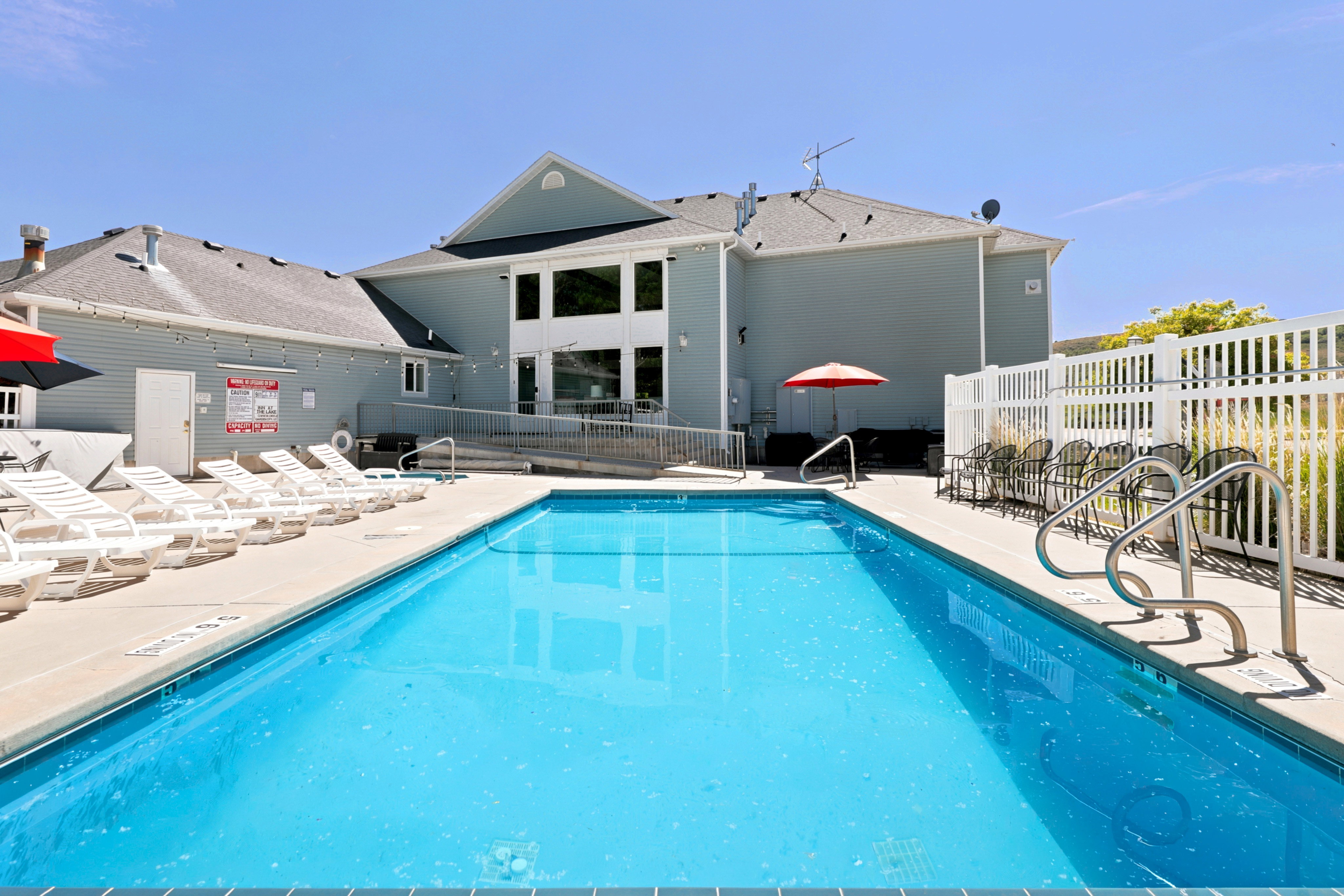 Outdoor swimming pool featuring a concrete deck, multiple lounge chairs, and a white picket fence