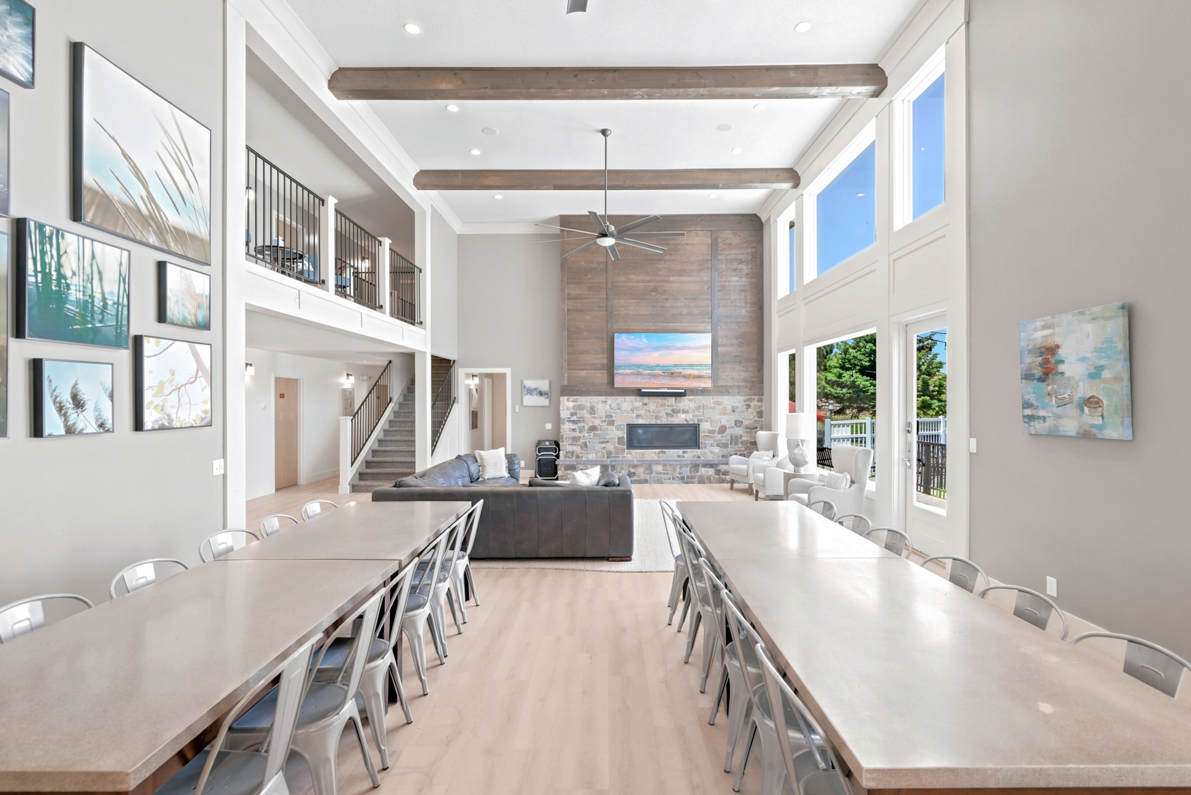 Two-story living area featuring a stone fireplace, wood-finish accent wall, exposed ceiling beams, and a ceiling fan