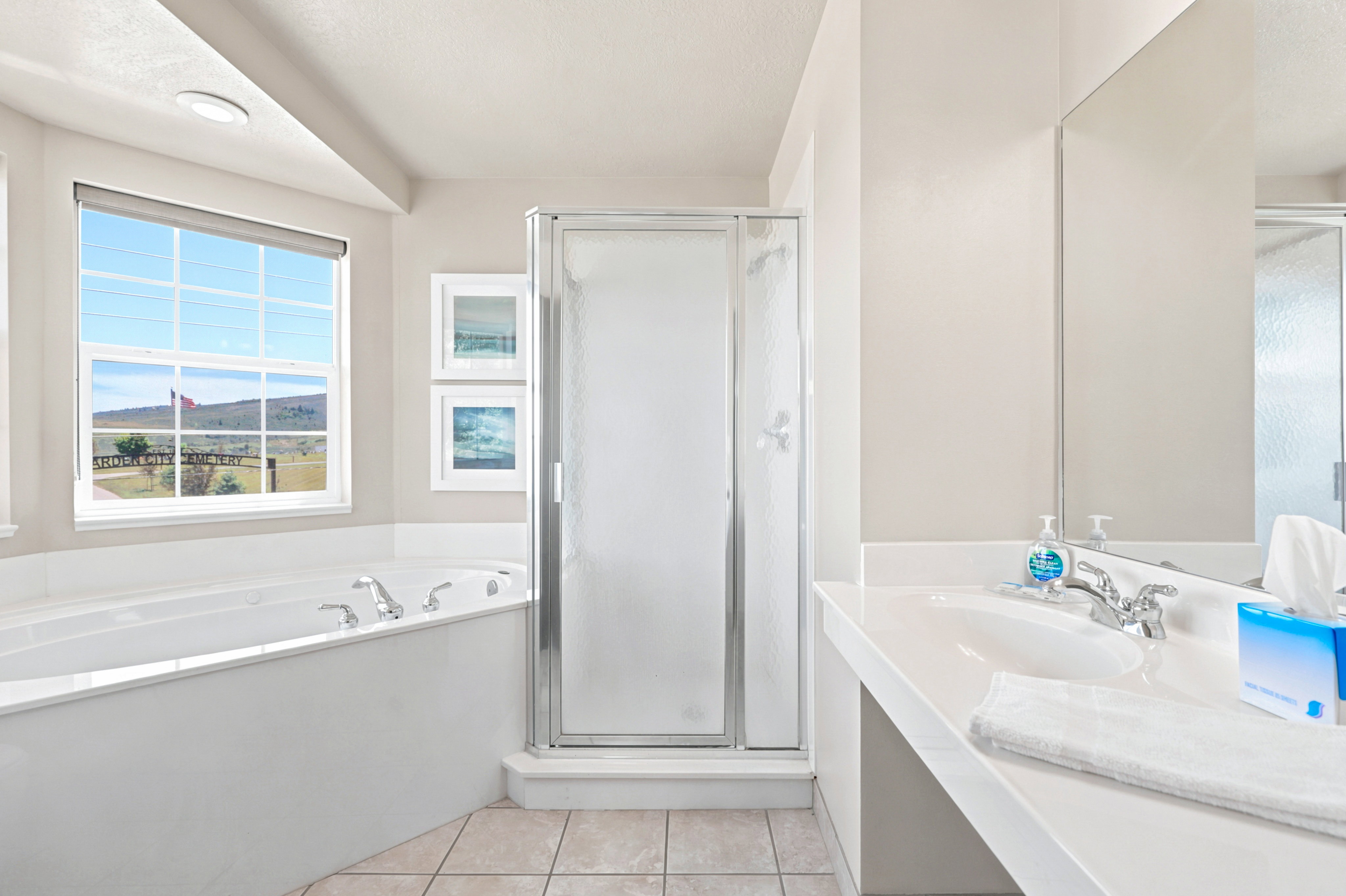 Bathroom featuring a built-in soaking tub, separate shower with frosted glass enclosure, single vanity with integrated sink, and an expansive window with outdoor scenery