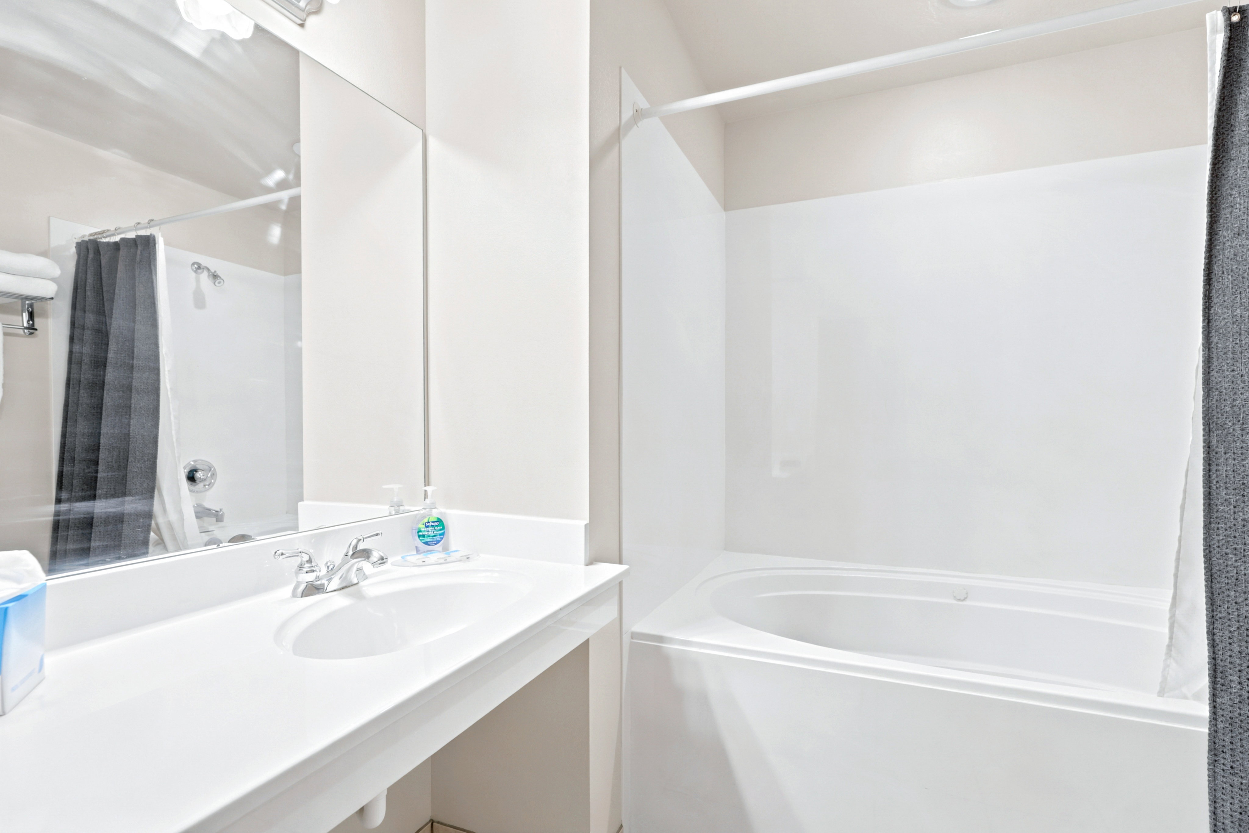 Bathroom featuring a built-in white bathtub, an integrated vanity sink with a laminate countertop, and a large wall-mounted mirror