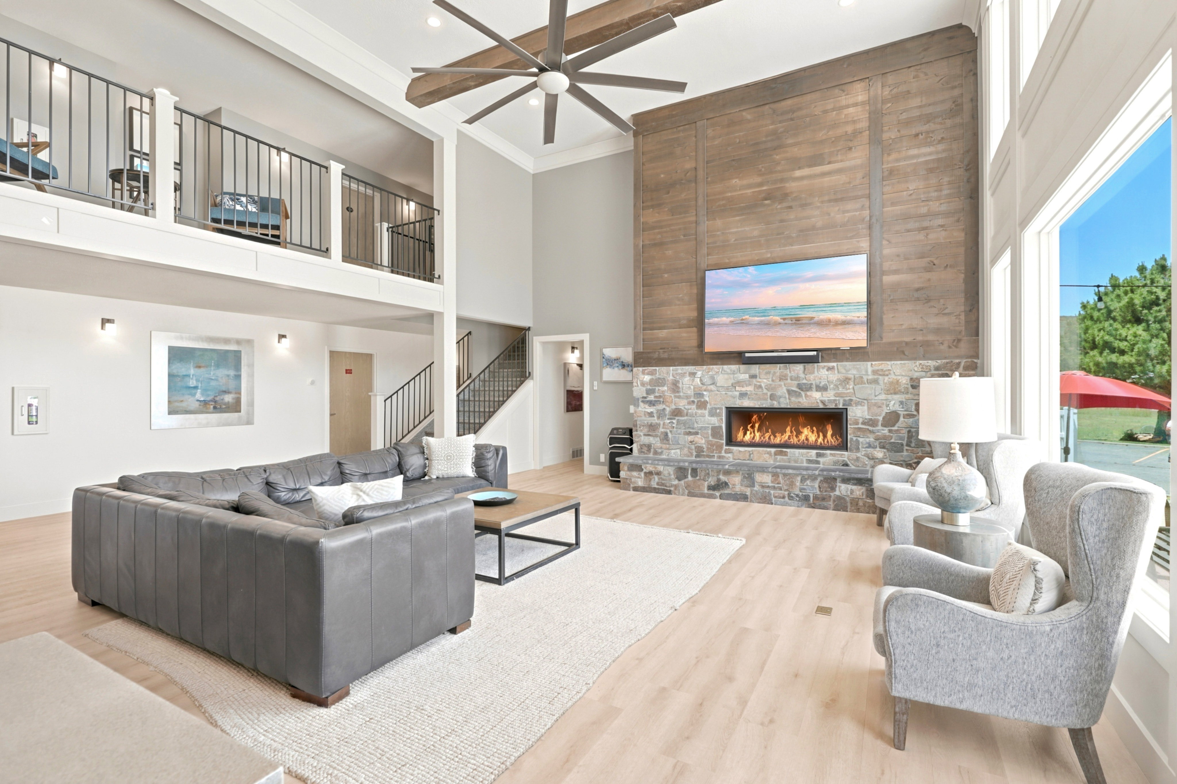 Vaulted ceilings featuring a large ceiling fan and a stone fireplace with a wood-finish accent wall