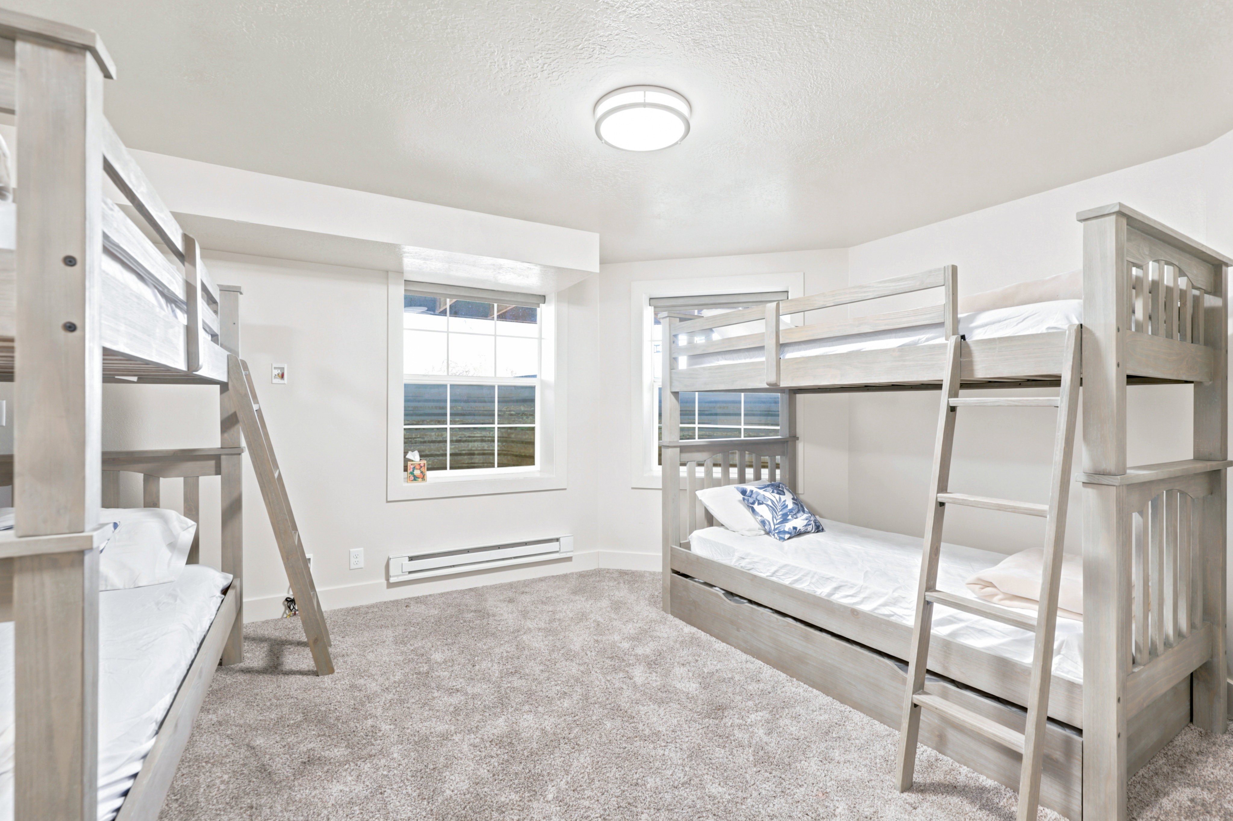 Bedroom featuring two bunk beds with ladders, soft grey carpeting, and two windows providing natural light