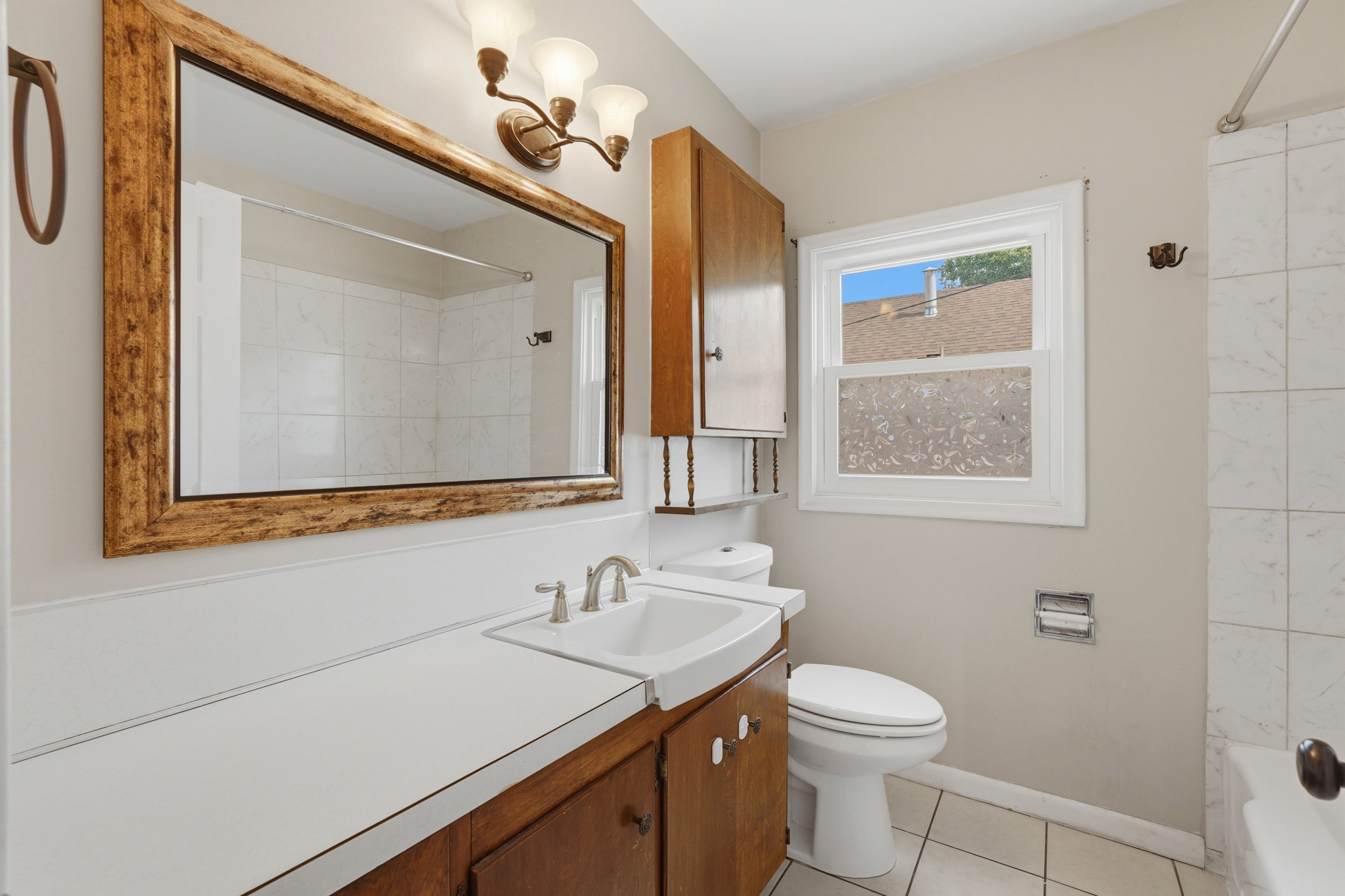 Bathroom featuring a vanity with wood-finish cabinetry and a white countertop, a rectangular mirror with a decorative frame, and a window providing natural light