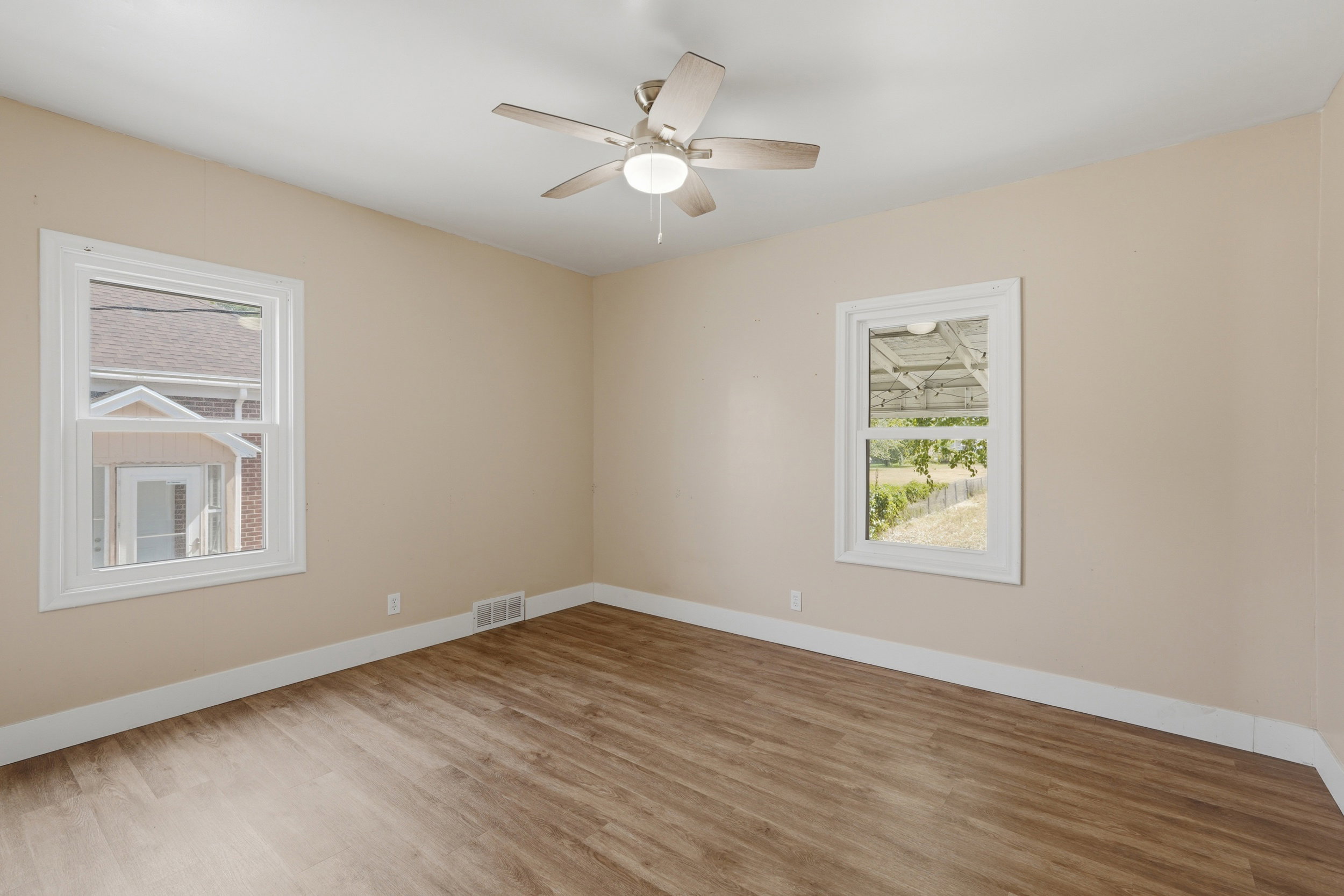 Room featuring wood-finish flooring, neutral wall paint, white baseboards, and two windows with white trim