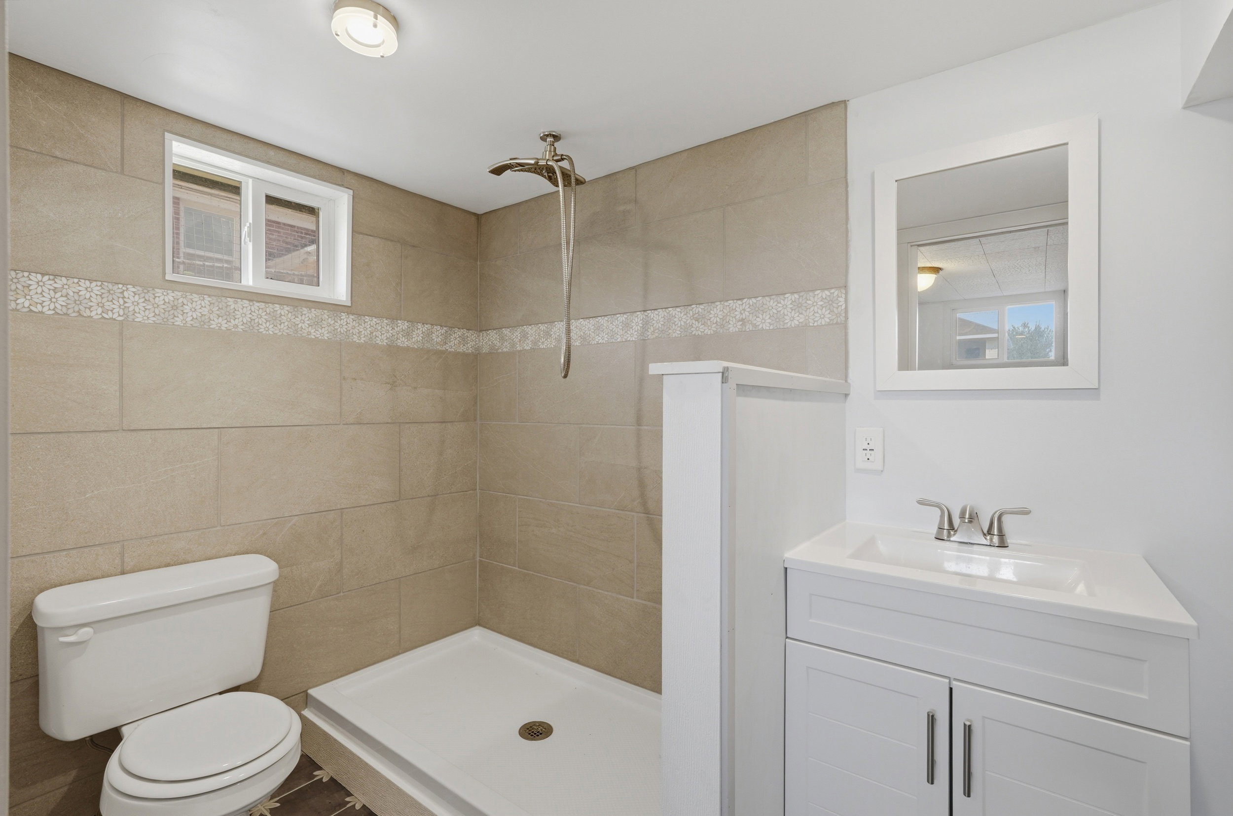 Shower with beige large format tile surround, decorative mosaic accent tile, and a rainfall showerhead