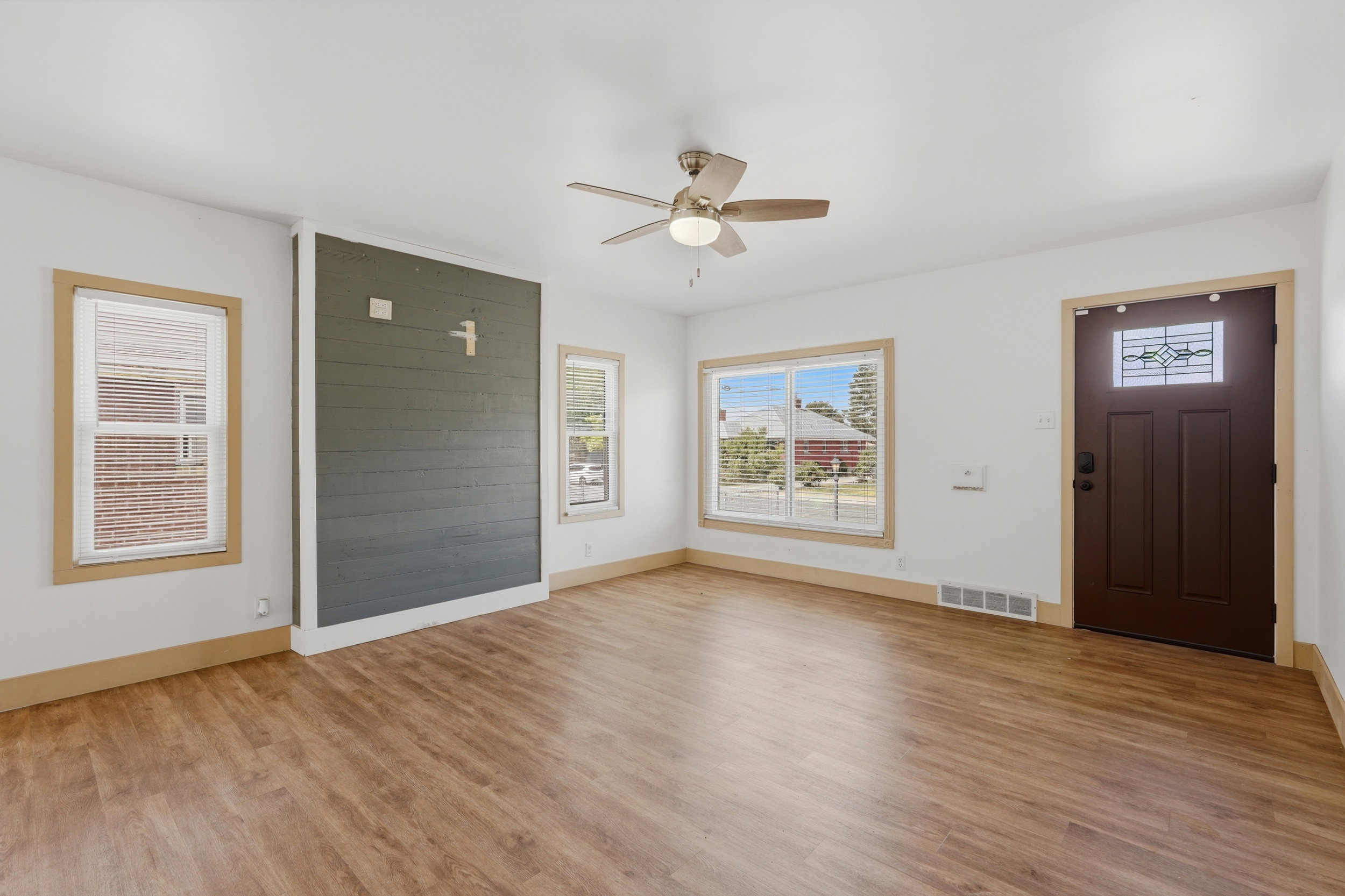 Spacious living area featuring wood-finish flooring, a contemporary ceiling fan, and a prominent accent wall