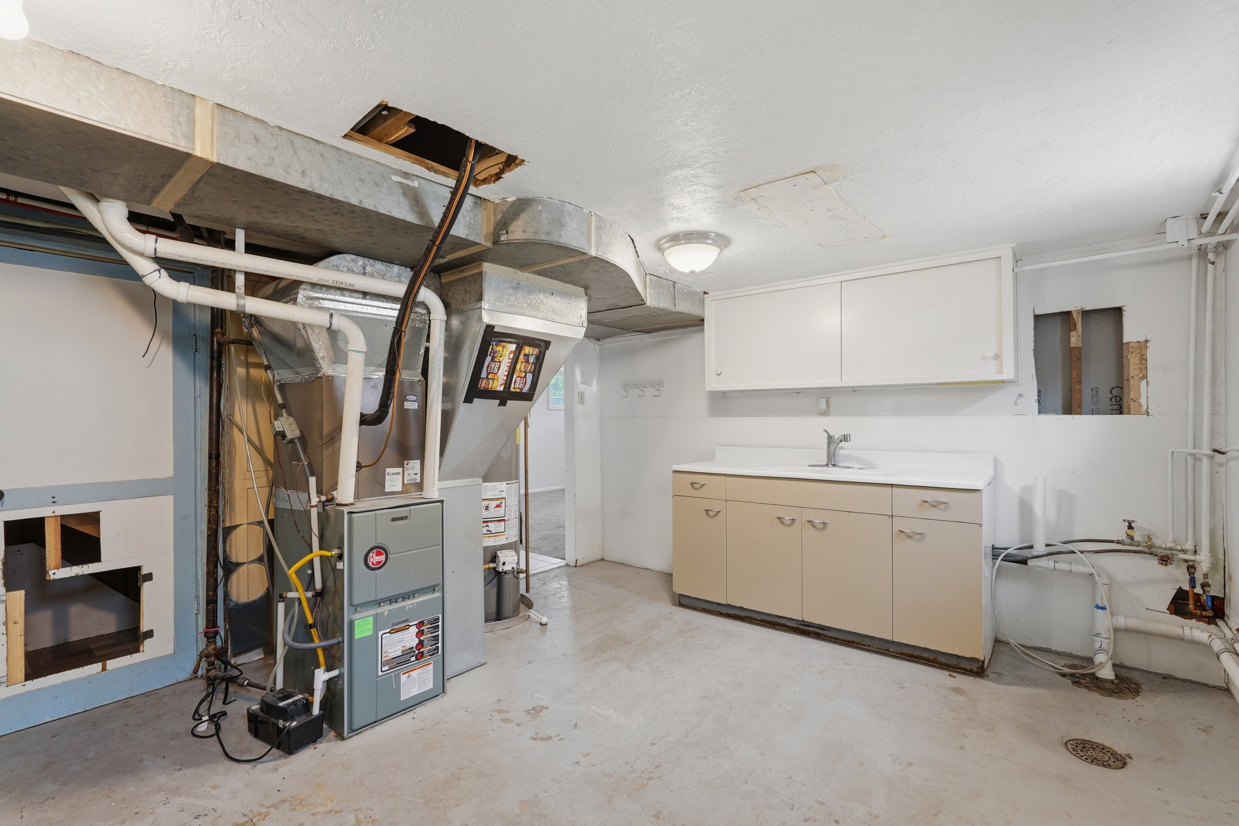 Utility area featuring a furnace system, exposed ductwork, a utility sink with base cabinetry, and overhead wall cabinets