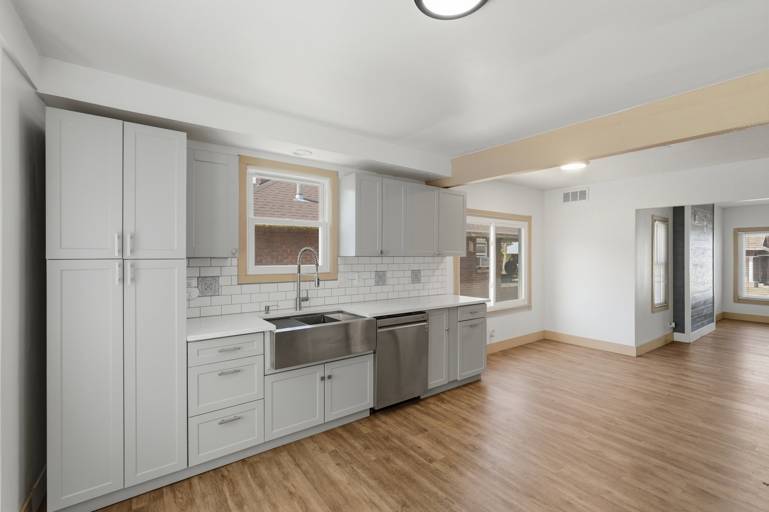 Kitchen featuring light gray cabinetry, white countertops, subway tile backsplash, a stainless steel farmhouse sink, and wood-finish flooring