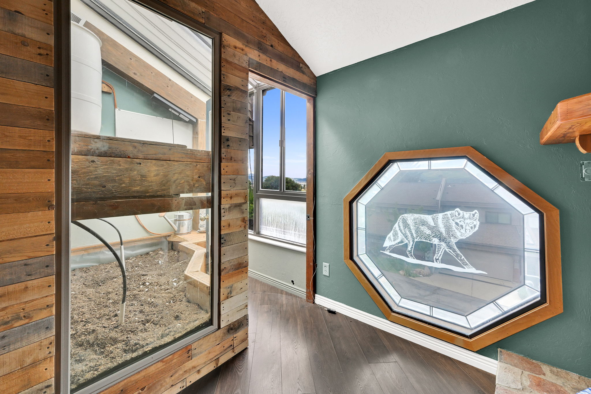 Interior space featuring wood-finish flooring, a decorative octagonal window with etched glass, and exposed wood plank wall paneling