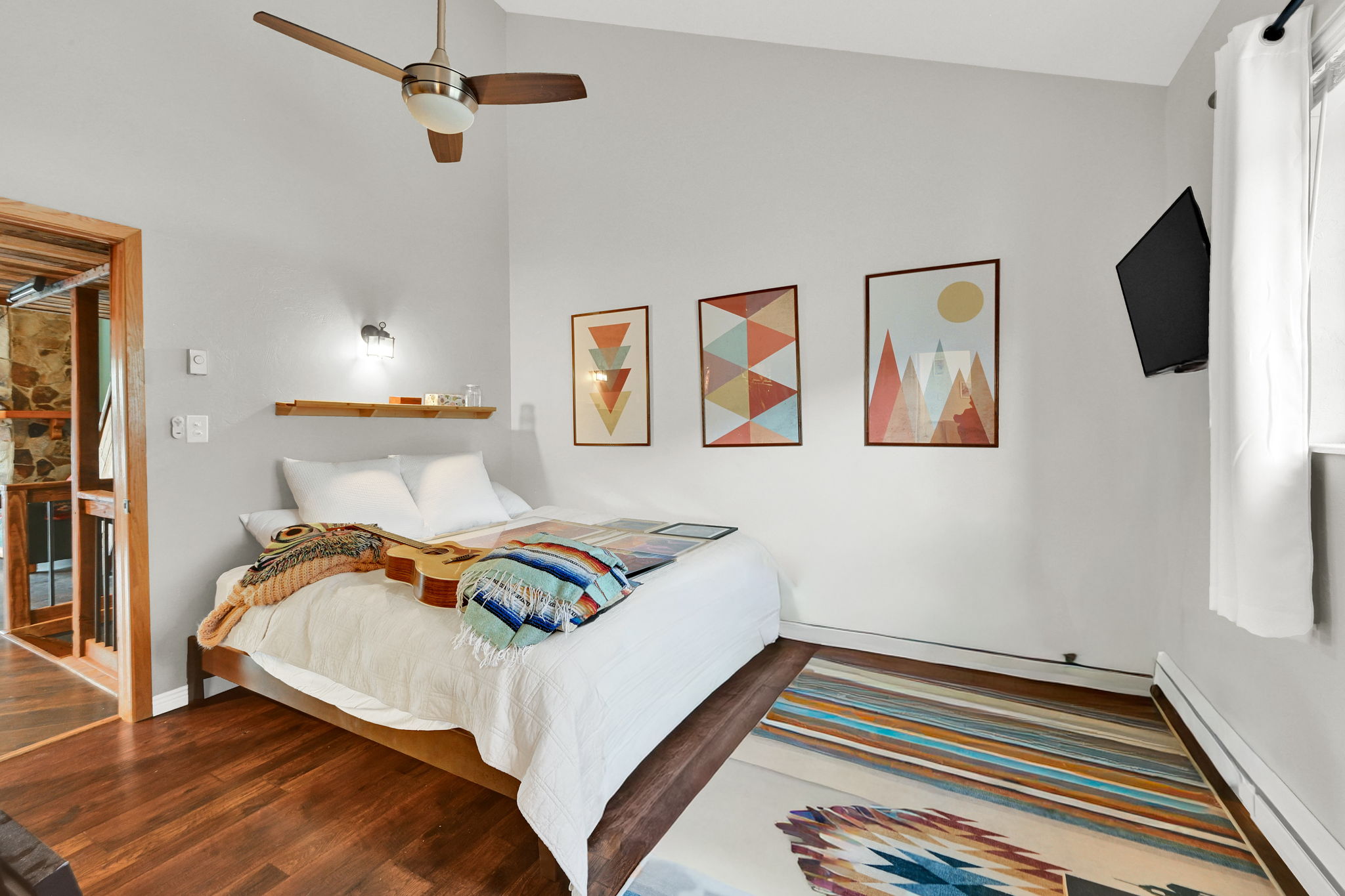 Vaulted ceiling with a ceiling fan, wood-finish flooring, wall-mounted light fixture, and a built-in wall shelf