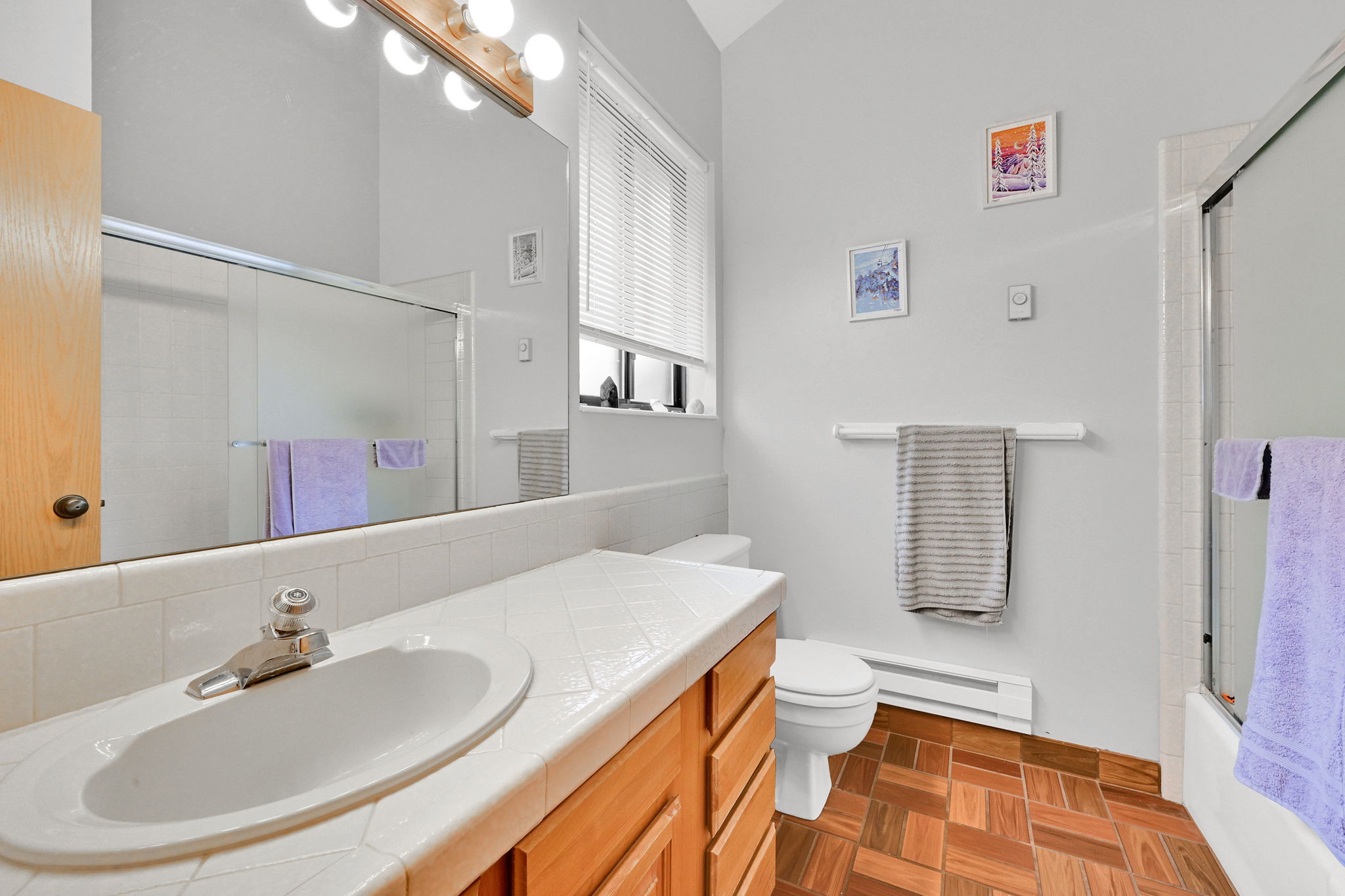 Bathroom featuring a wood-finish vanity with an integrated sink, tile countertop, and a large wall-mounted mirror