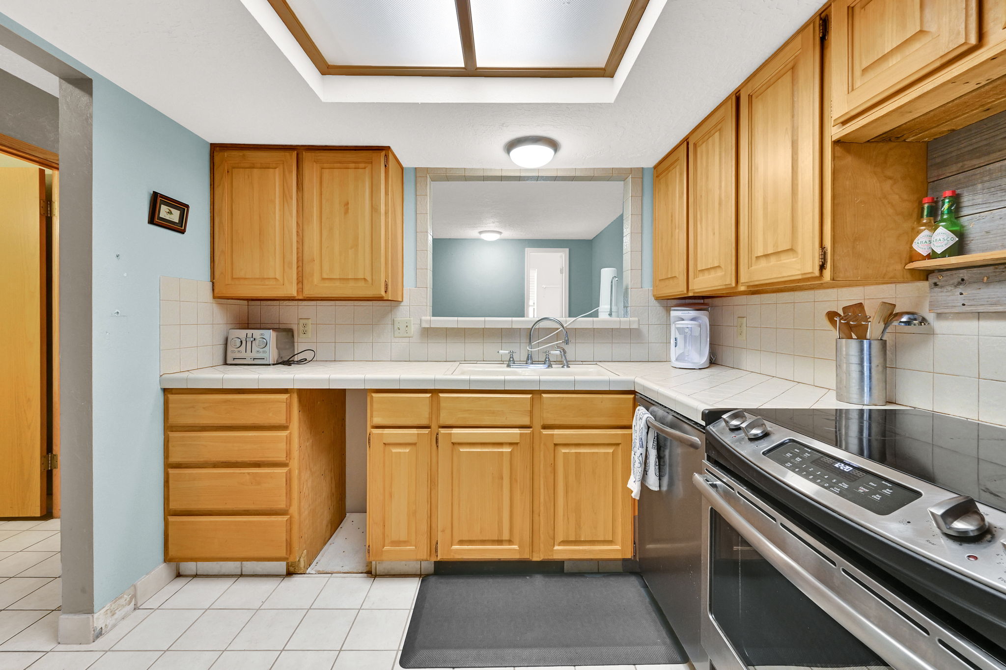 Kitchen featuring light wood cabinetry, white tile countertops, and a full tile backsplash