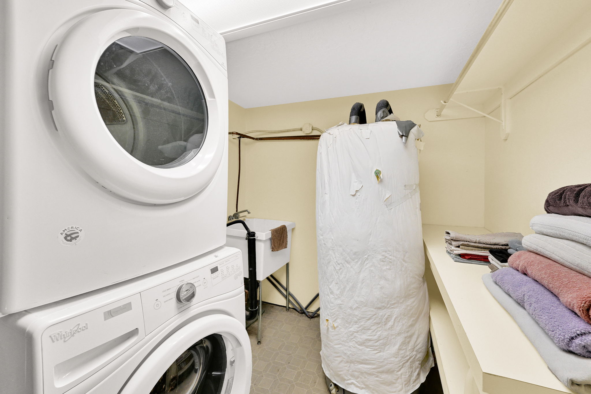 Dedicated laundry area featuring a stacked washer and dryer, utility sink, and built-in shelving for organization
