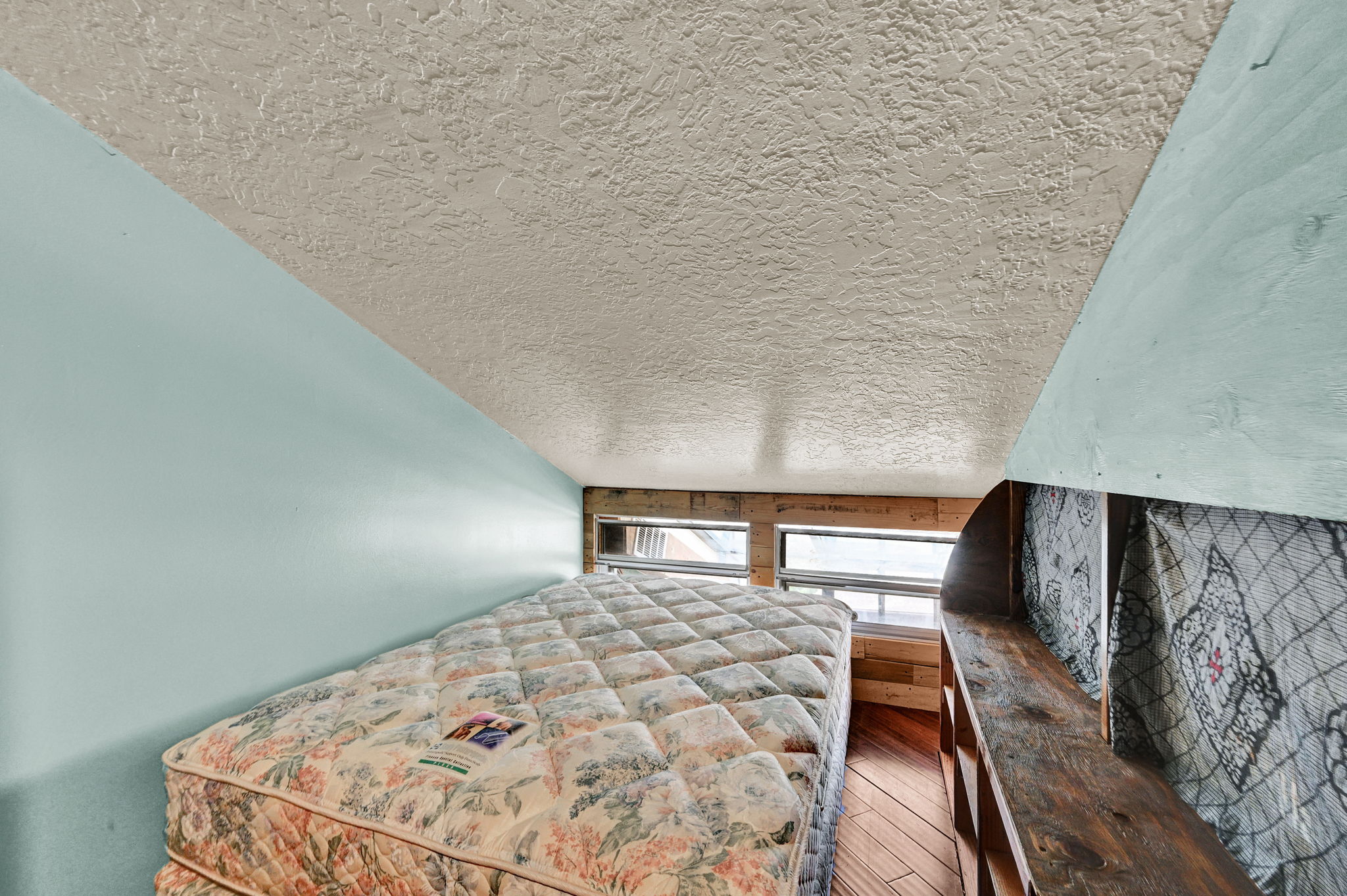 Sloped ceiling space featuring a textured ceiling finish, light blue wall paint, and wood-finish flooring