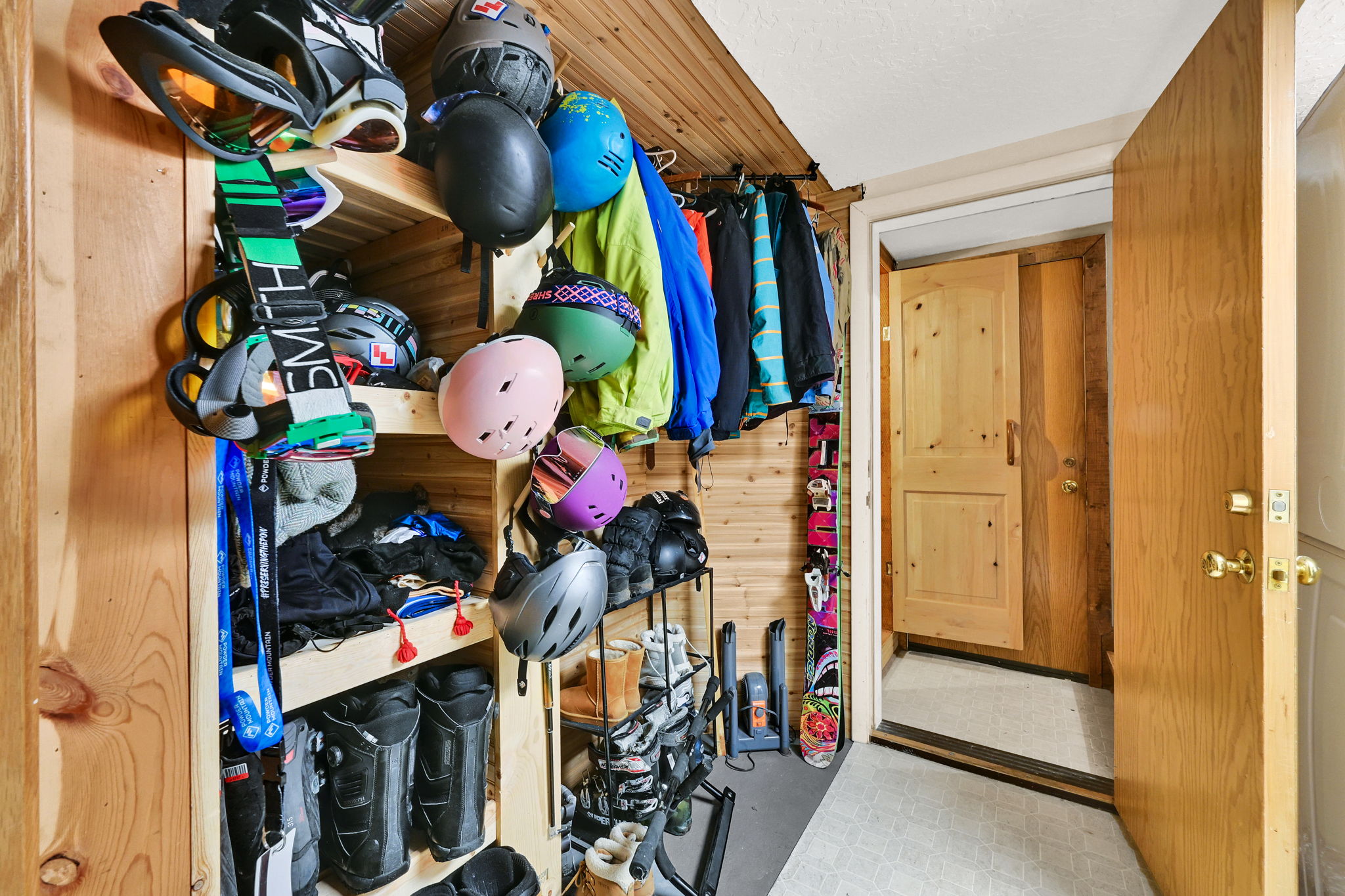 Entryway storage featuring wood-paneled walls and ceiling, built-in shelving, clothing rod, and a solid wood door with brass hardware