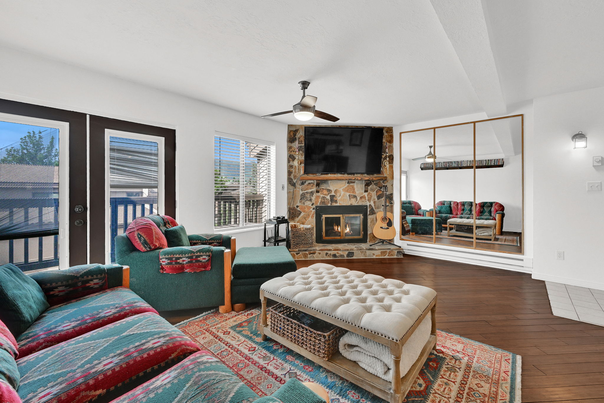 Living area featuring wood-finish flooring, a stone-faced fireplace with a hearth, and built-in mirrored wall panels