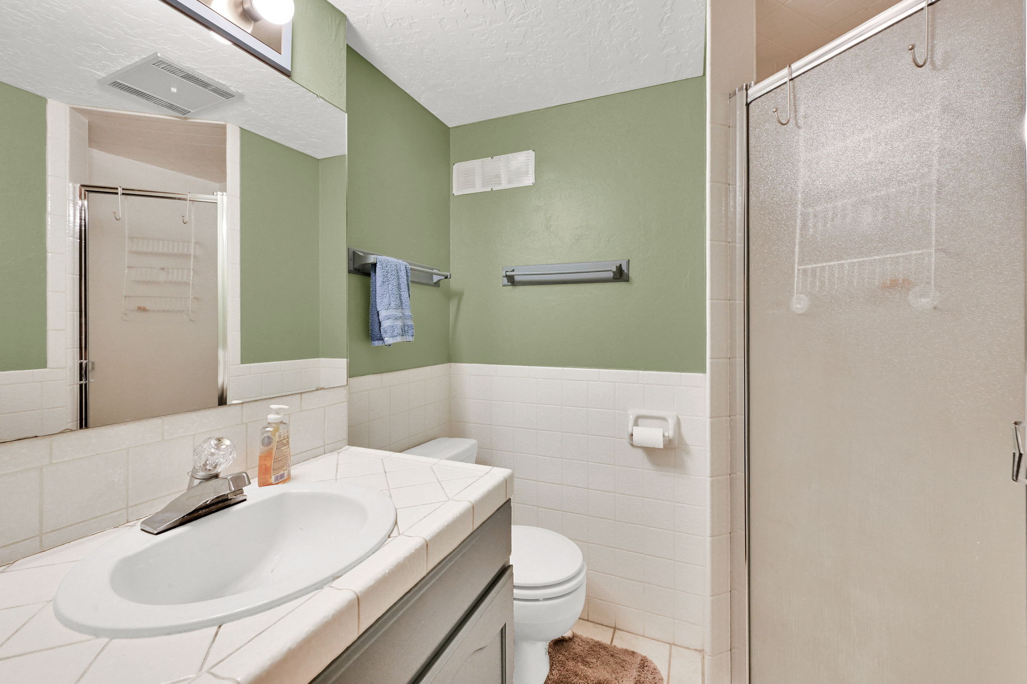 Bathroom featuring a vanity with a drop-in sink, white tiled countertop, large mirror, and a shower with a frosted glass enclosure