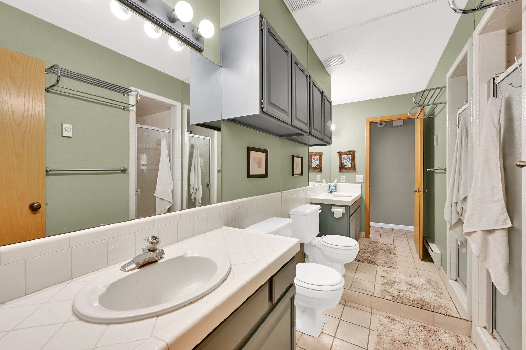 Bathroom featuring an extended vanity with tile countertop, integrated sink, and full-wall mirror