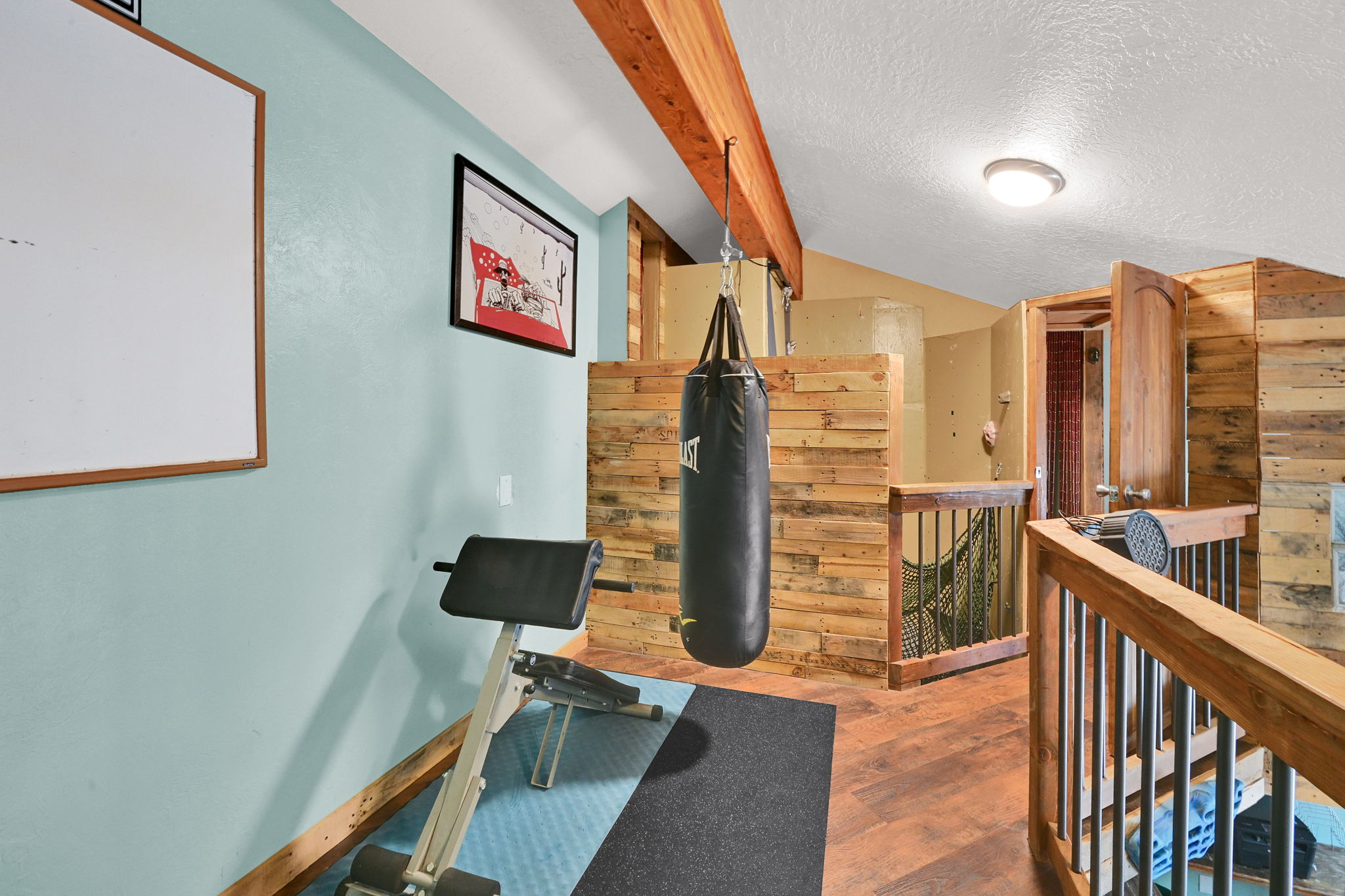 Loft space featuring wood-finish flooring, exposed wood beams, and a wood plank half-wall with iron balusters