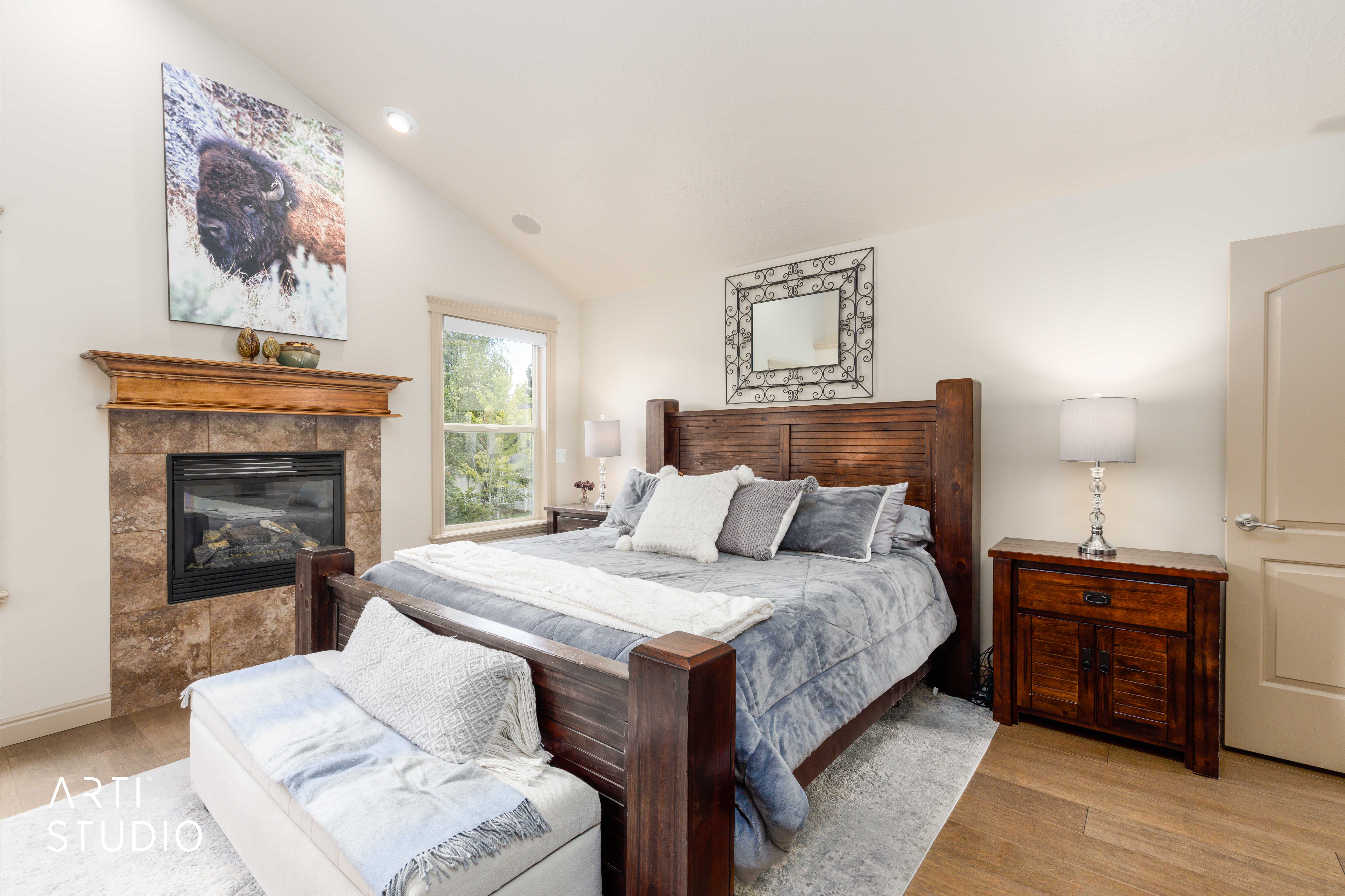 Primary bedroom with vaulted ceilings featuring gas fireplace with wood mantel, large window, wood floors