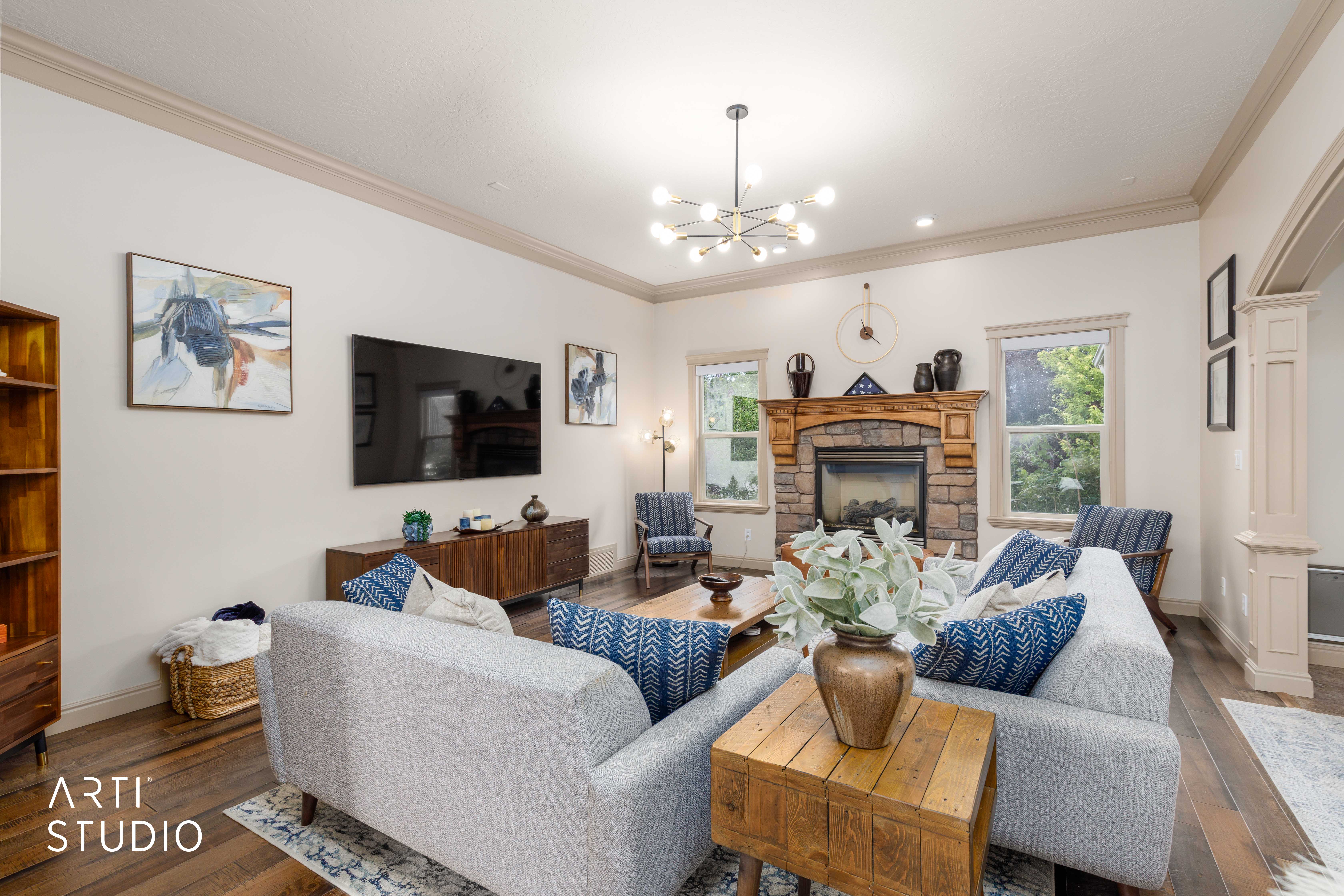 Living area featuring a stone-clad fireplace with a wood mantel, wood floors, and a modern chandelier