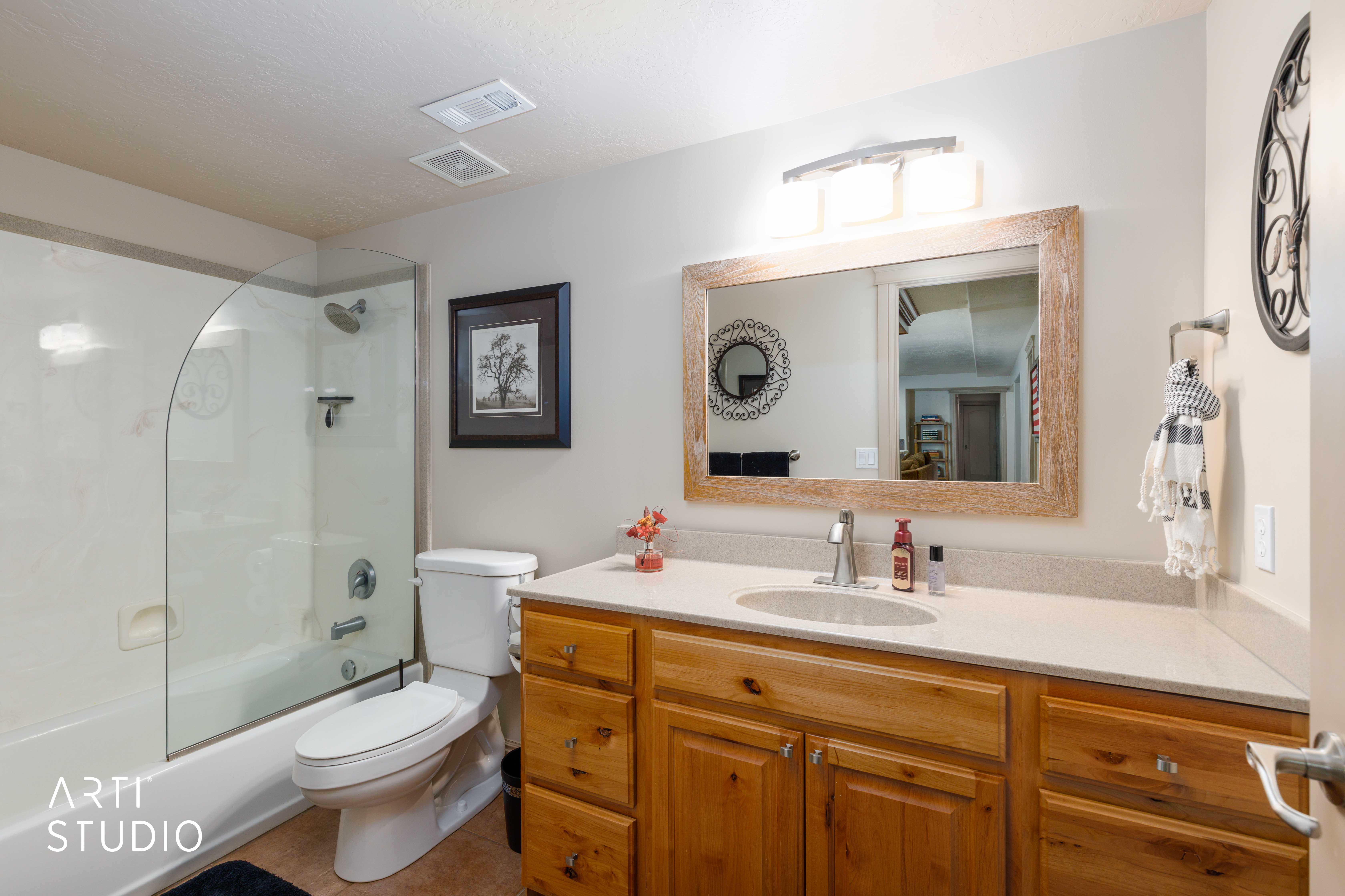 Bathroom featuring a combination shower and tub with a curved glass enclosure, a toilet, a single vanity with wood cabinetry